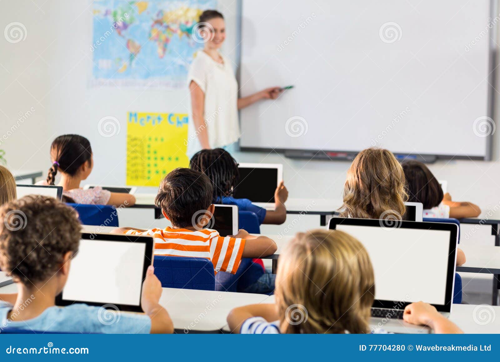 Schulkinder, die digitale Tabletten gegen den weiblichen Lehrer unterrichtet sie verwenden. Schulkinder, die digitale Tabletten gegen den weiblichen Lehrer unterrichtet sie im Klassenzimmer verwenden