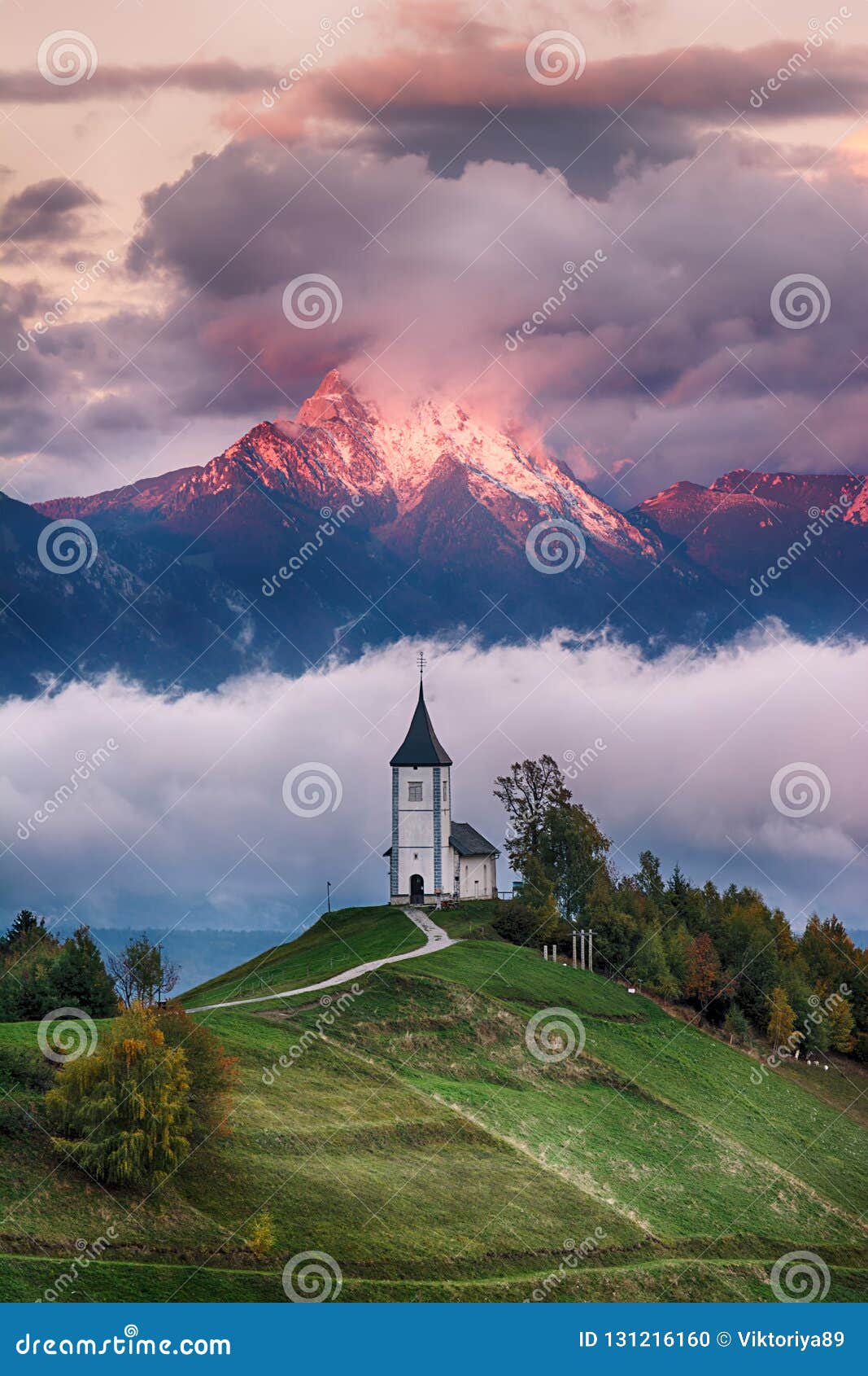 Schöne Sonnenaufganglandschaft der Kirche Jamnik in Slowenien mit bewölktem Himmel. Schöne Sonnenaufganglandschaft der Kirche Jamnik in Slowenien auf grünem Hügel mit blauem bewölkter Himmel- und Gebirgshintergrund