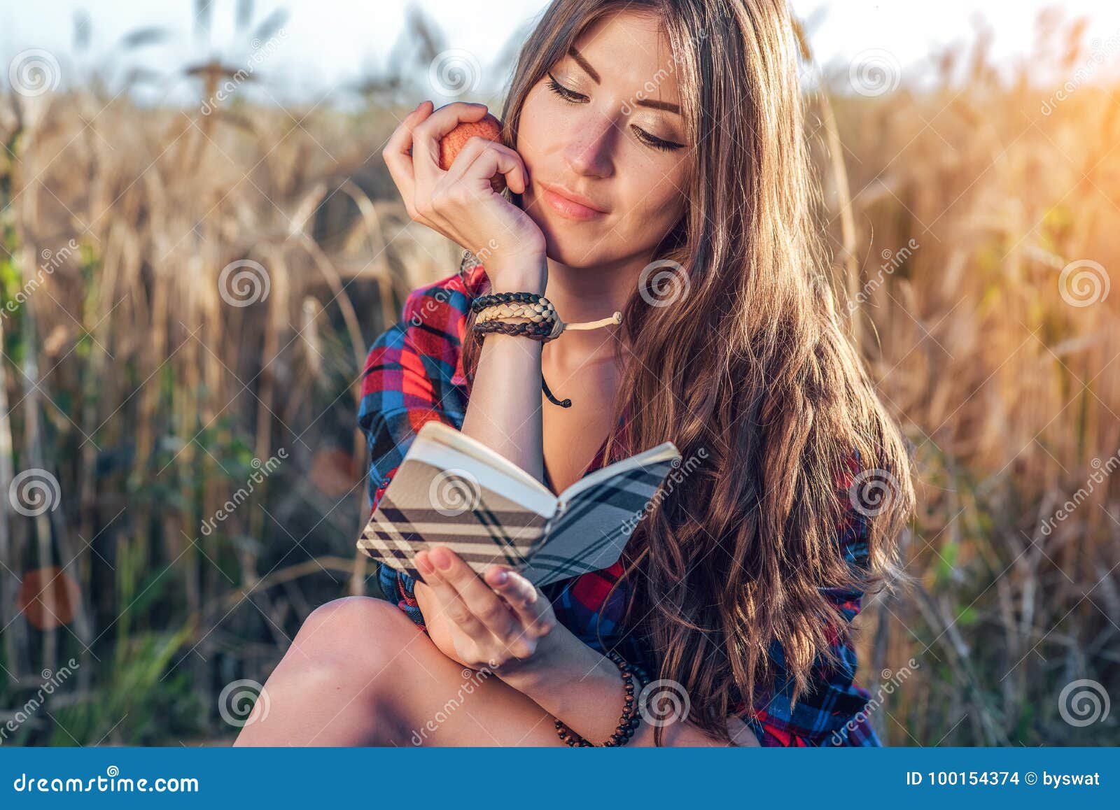 Schönes Studentinfeld In seinem Handapfel Neue Ideen des Konzeptes draußen Sommer in der Natur In der Hand Notizbuch, lang. Schöne Studentin auf dem Gebiet In seiner Hand ist ein Apfel Neue Ideen des Konzeptes draußen Sommer in der Natur In seiner Hand ein Notizbuch, langes Haar Kluge Ideen Inspiration durch Kreativität Liest das Tagebuch