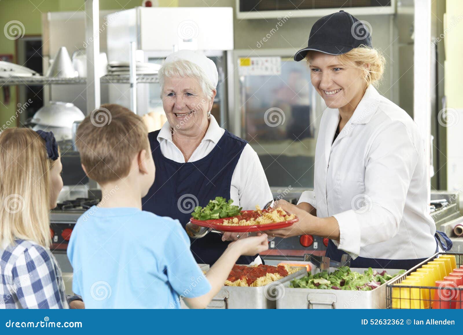 Schüler in der Schulcafeteria, die das Mittagessen von den Abendessen-Damen gedient wird. Schüler in der Schulcafeteria, die von den Abendessen-Damen gedient wird