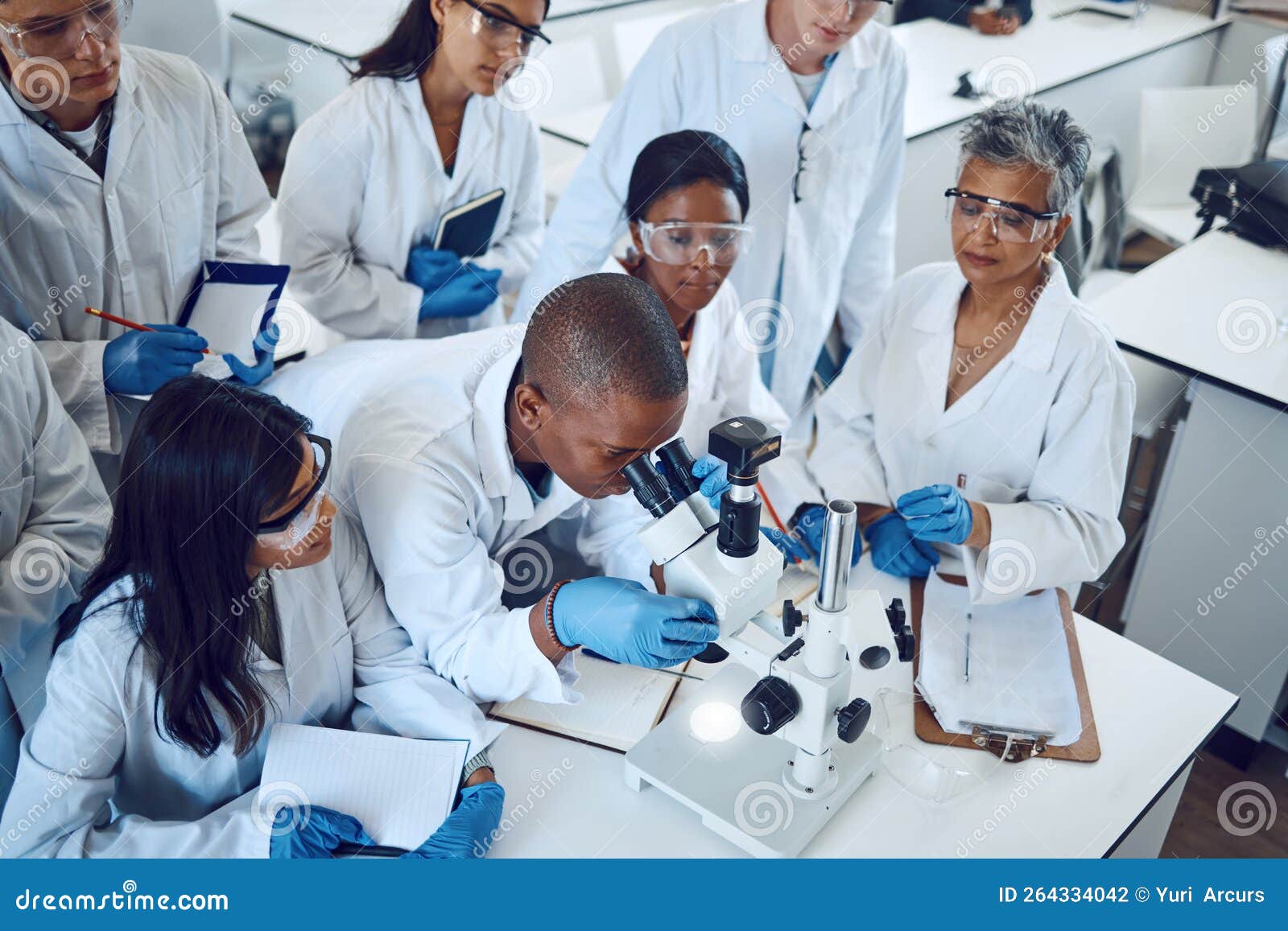 A mentor guiding students in a medical laboratory, using a microscope for pharmaceutical research and education.