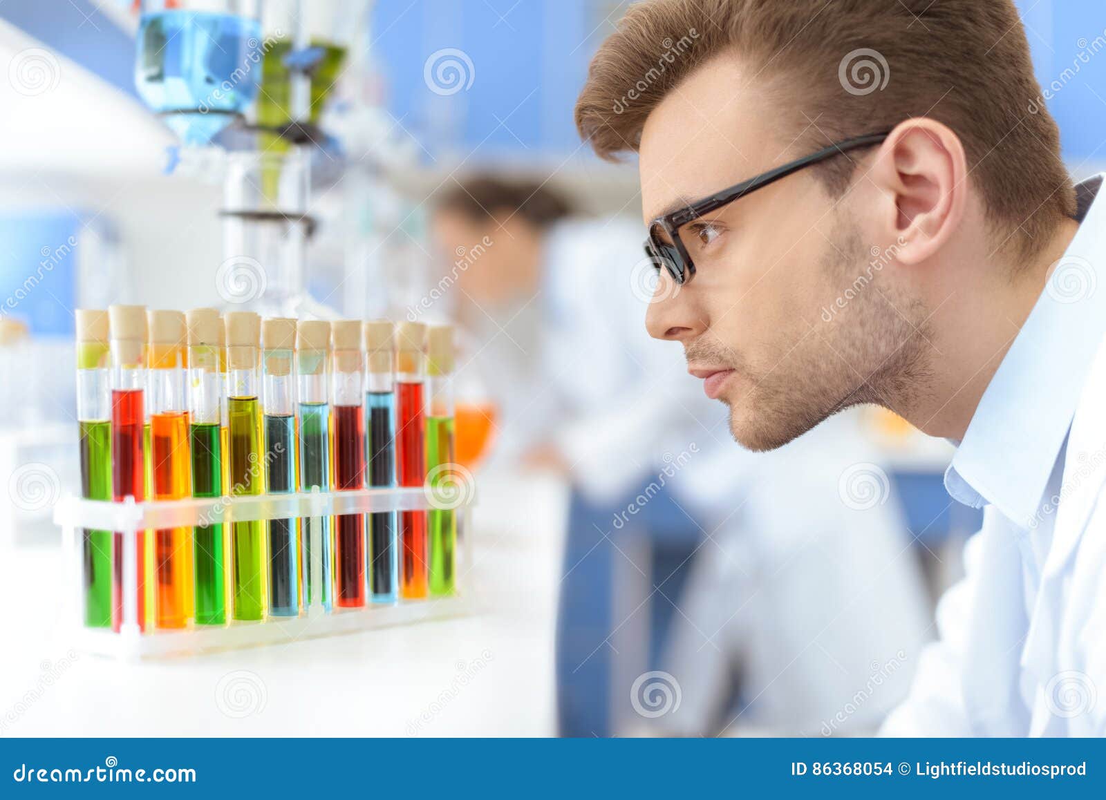 scientist in eyeglasses looking at test tubes with reagents in lab