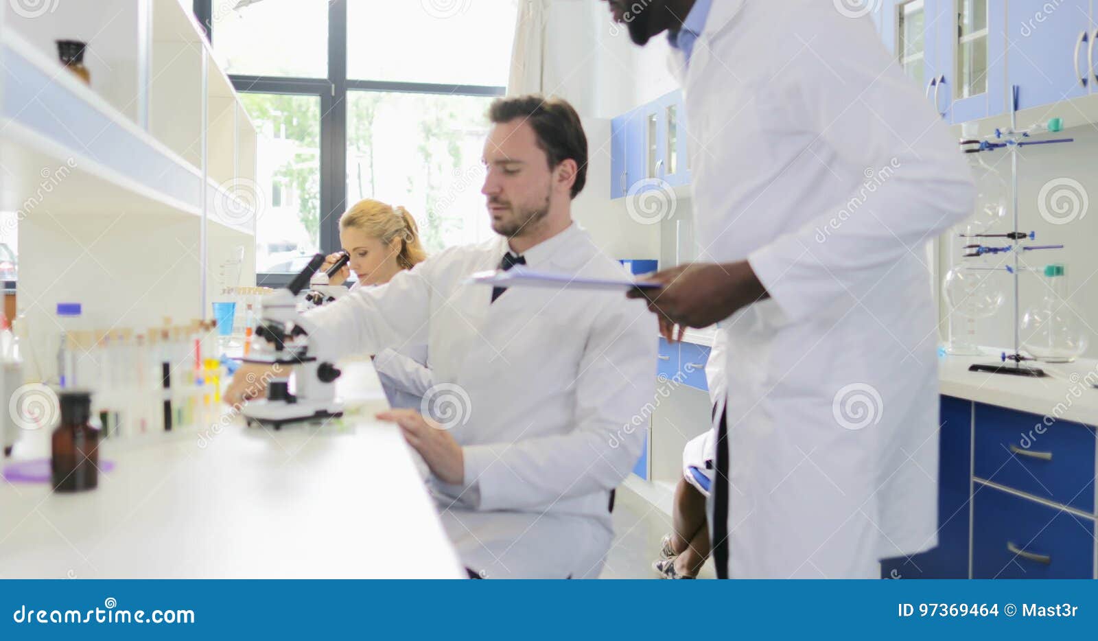 Scientist Man Examining Plant Example with Microscope Working in Laboratory with Group