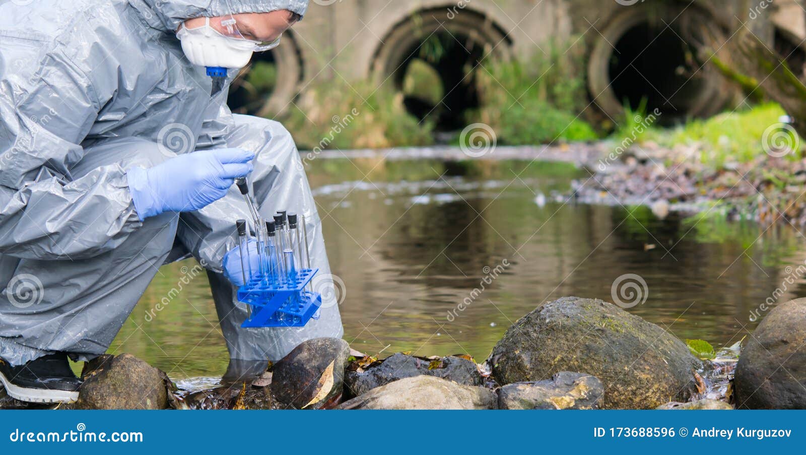 a scientist in a protective suit and mask, collects a sample of water in test tubes, against the background of drain pipes, there