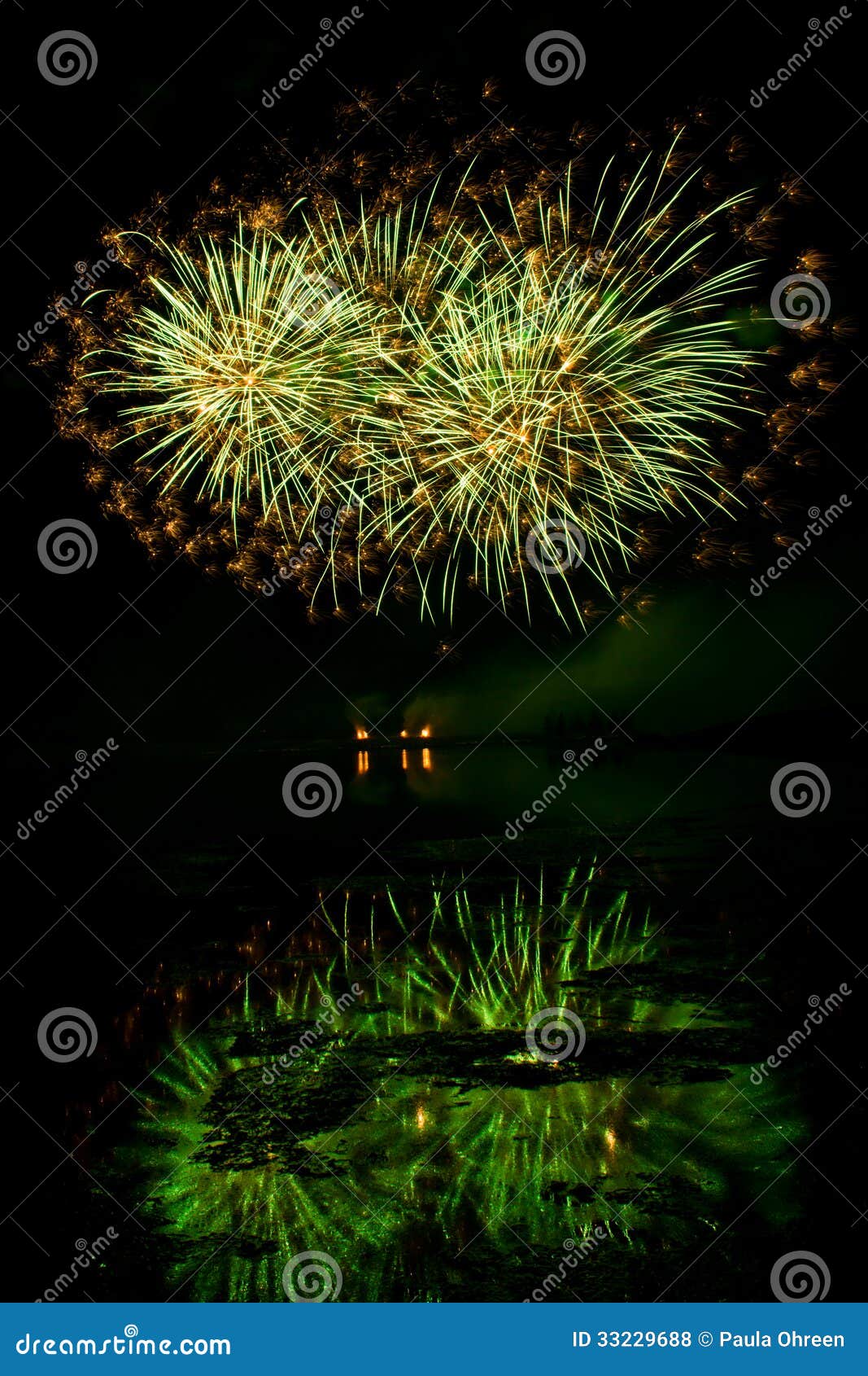 Gli scoppi dei fuochi d'artificio verdi ed arancio hanno riflesso in un lago oscuro