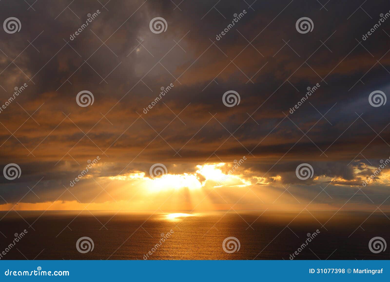 sunbeams through storm clouds over ocean by golden sunrise