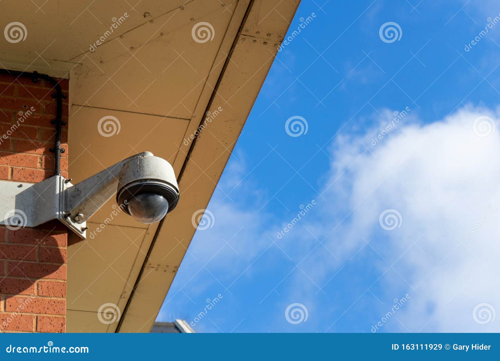 A Security Camera on a Wall with Blue Sky in the Background Stock Image