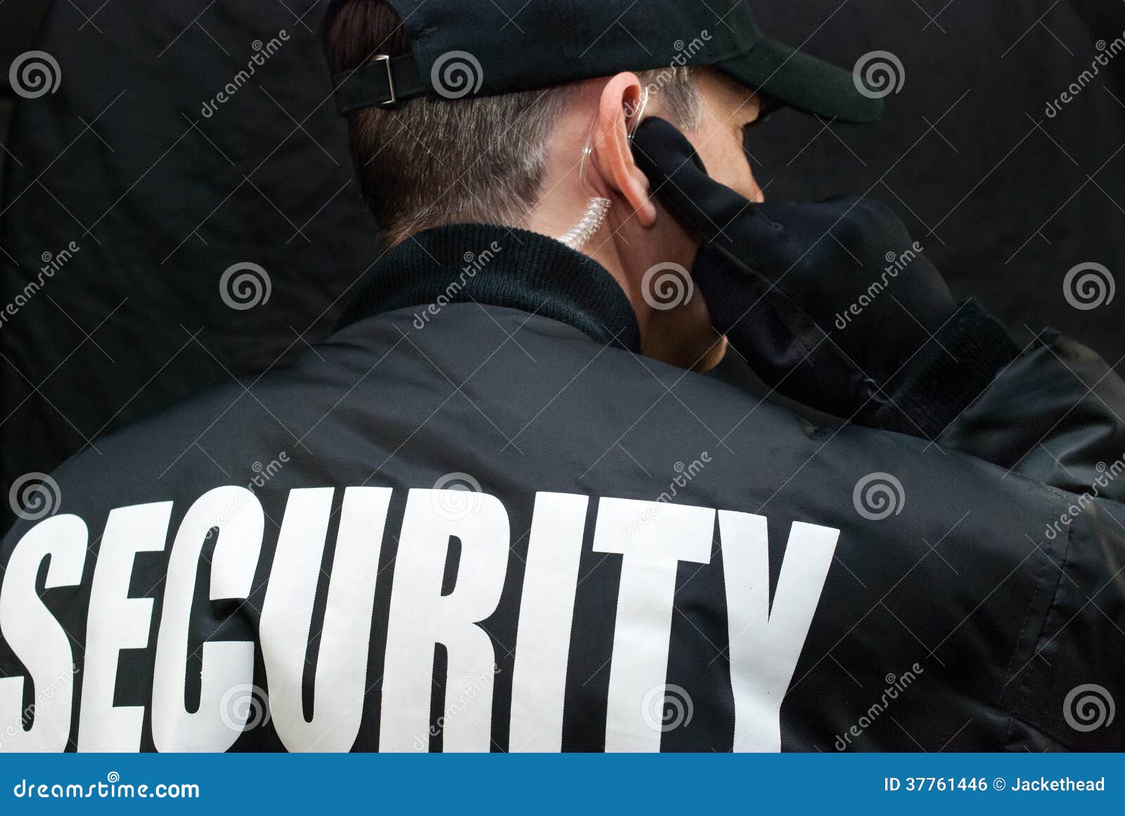 security guard listens to earpiece, back of jacket showing