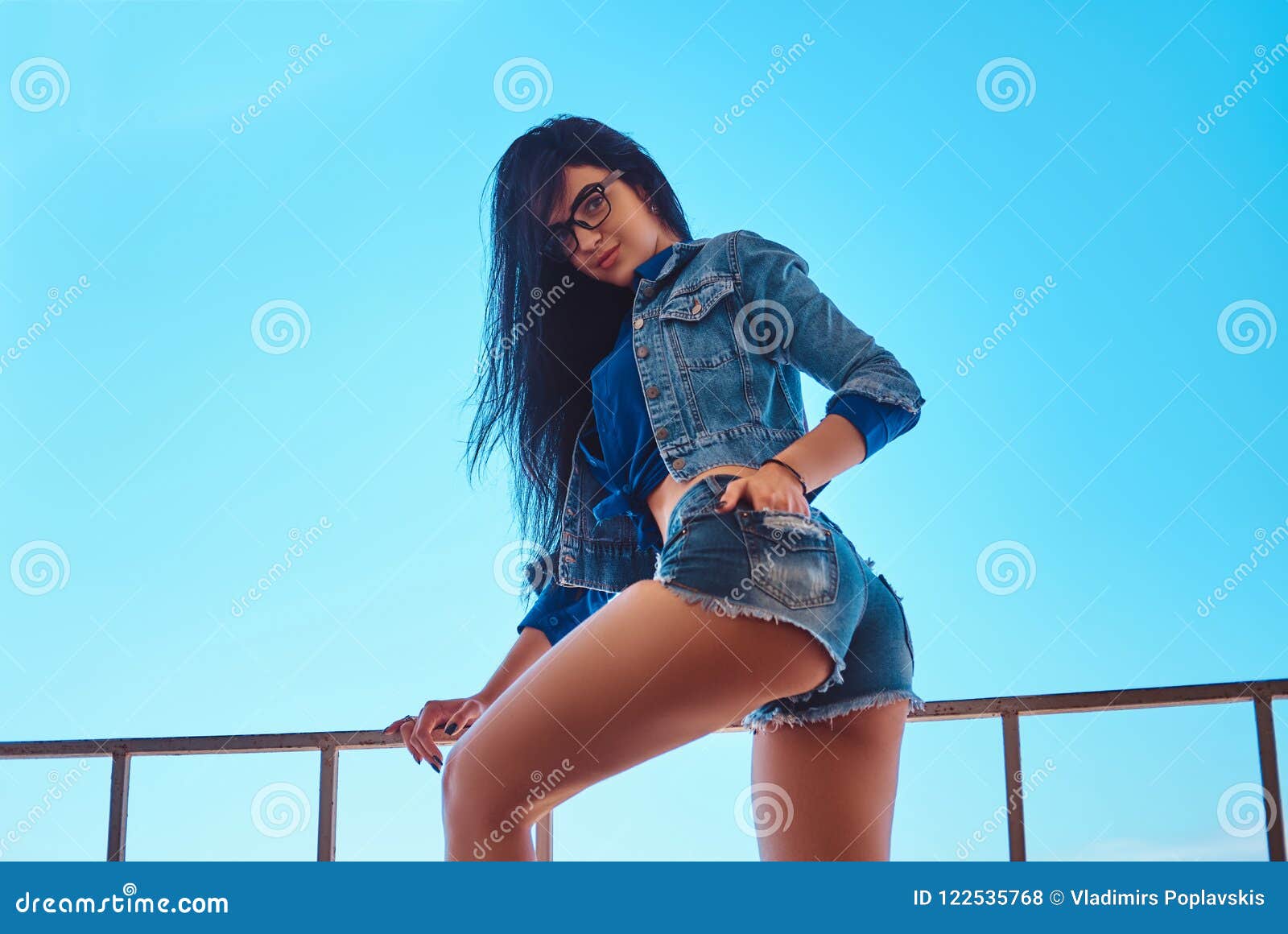 Seductive Brunette Girl Wearing Short Shorts and Jeans Jacket Posing while  Sitting on Guardrail Against a Sky Stock Photo - Image of posing, cool:  122535768