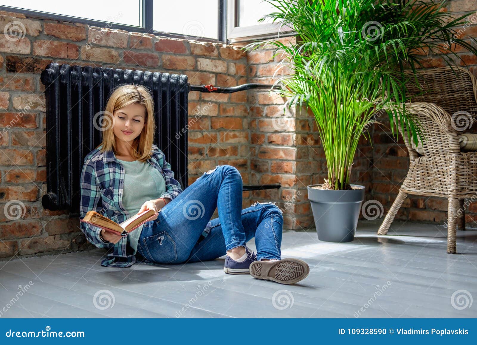 Seduta femminile bionda sul pavimento e sulla lettura un libro. Seduta femminile bionda casuale attraente sul pavimento e sulla lettura un libro in salone