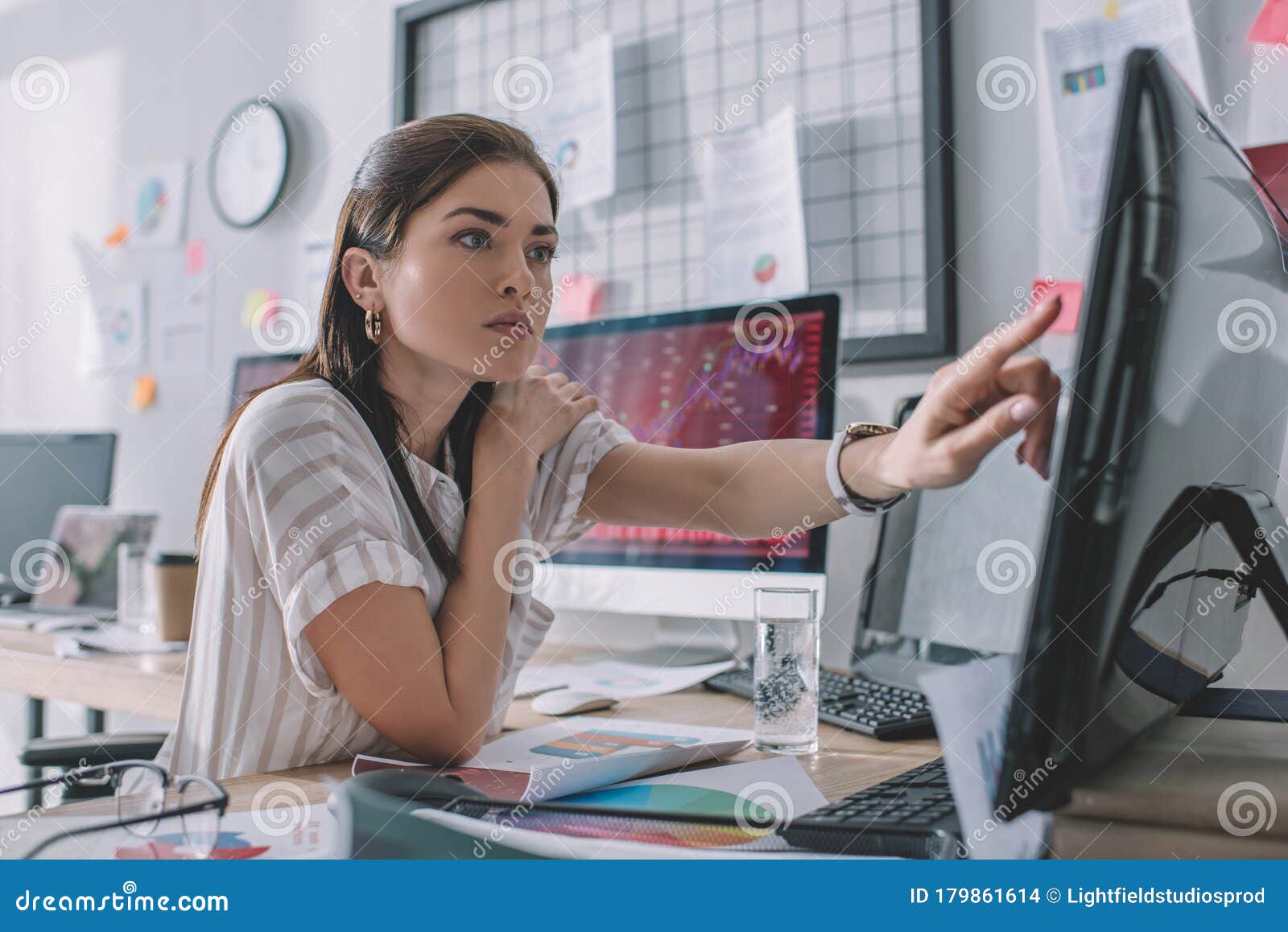selective focus of data analyst pointing with finger at computer monitor near papers and glass of water