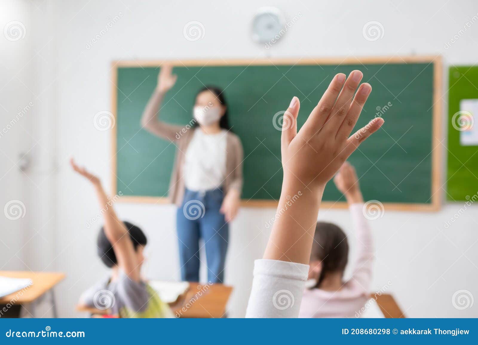 selective focus on hand. children or schoolkids or students raising hands up with asian teacher wearing protective face mask in