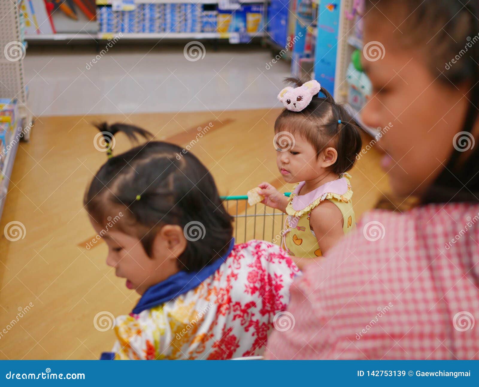 selective focus of little asian baby girl  furthest  looking and standing in a shopping cart with her sister