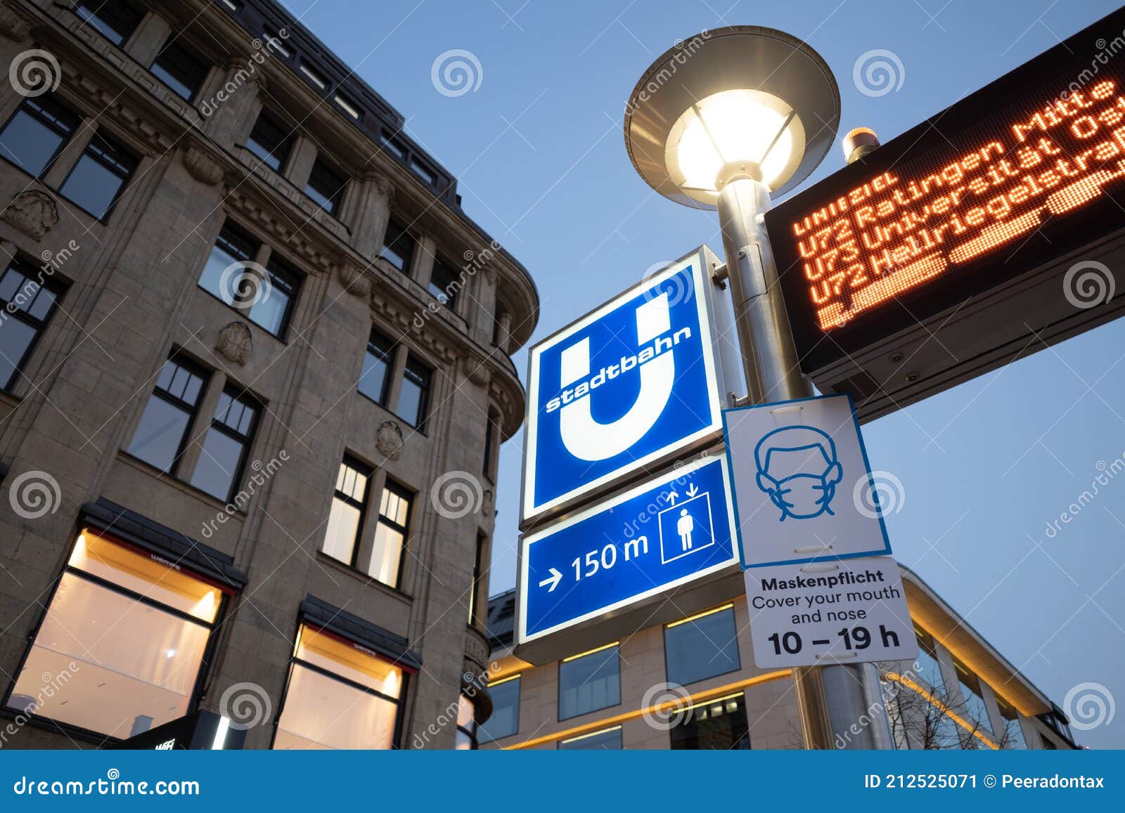 protective face mask signage under ubahn sign at entrance to underground metro train station.