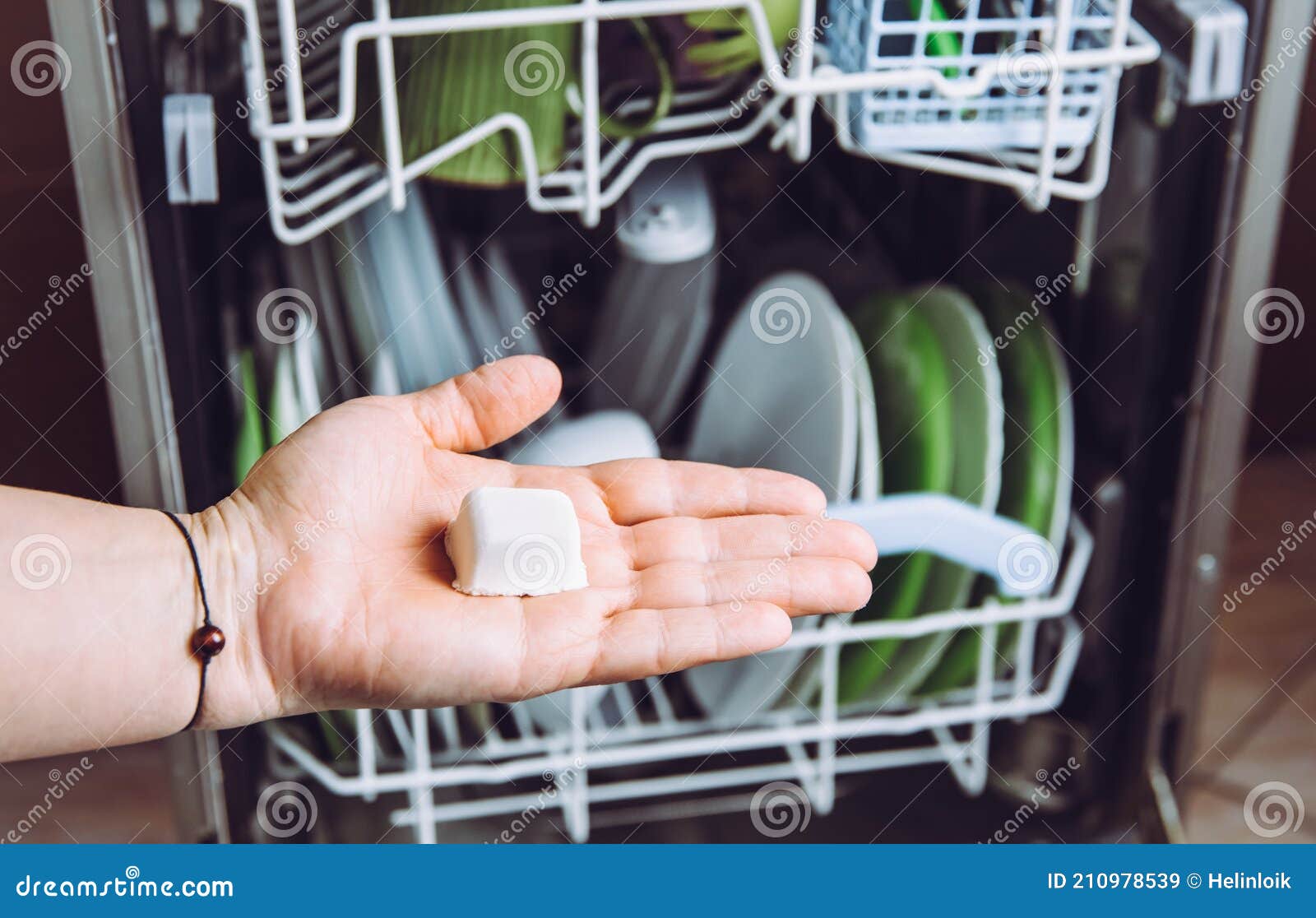 selective focus on woman hand, holding homemade natural dishwasher pod defocus dishes in dishwasher on background.