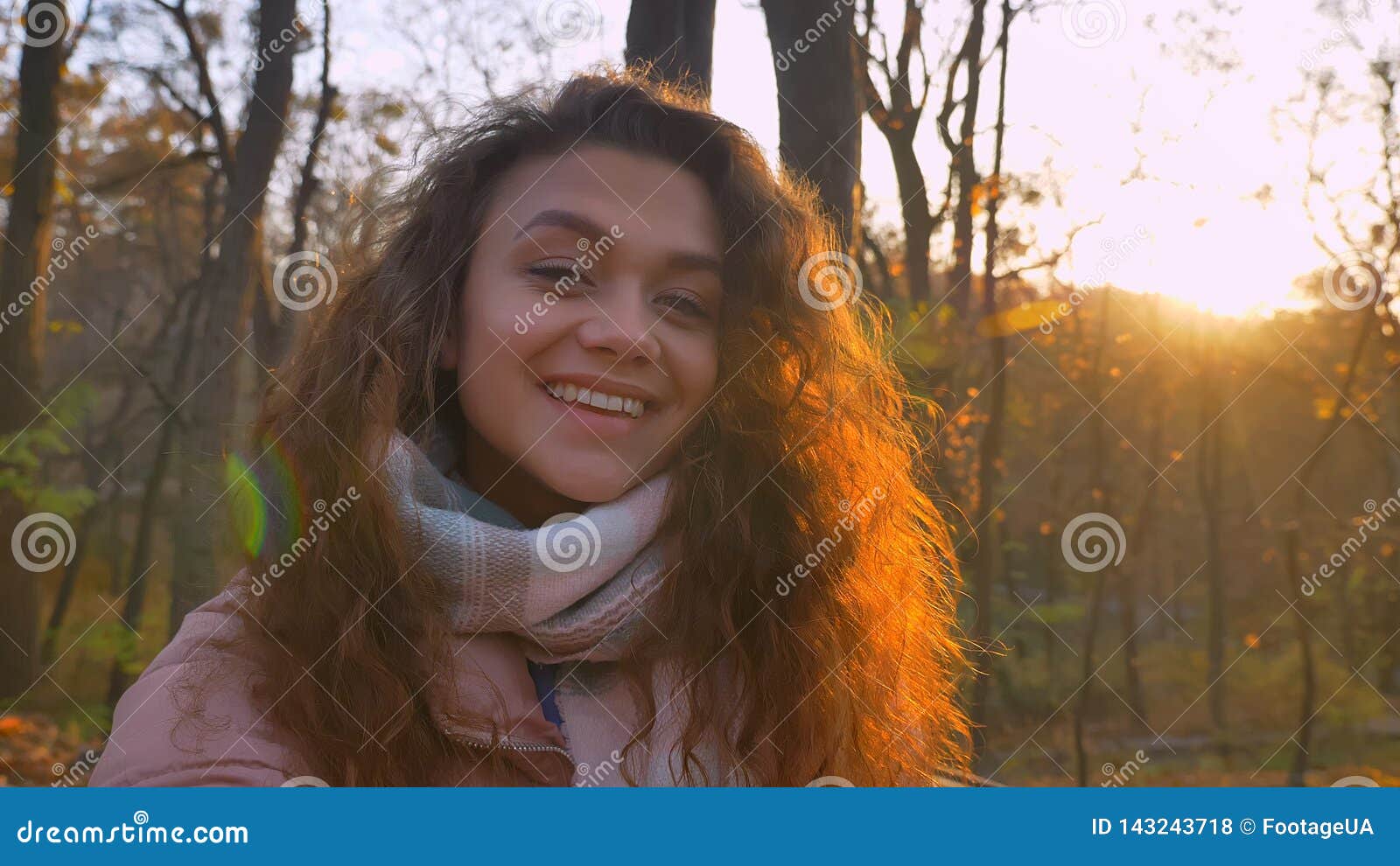 selfie-photo of curly-haired caucasian girl watching smilingly into camera in sunny autumnal park.