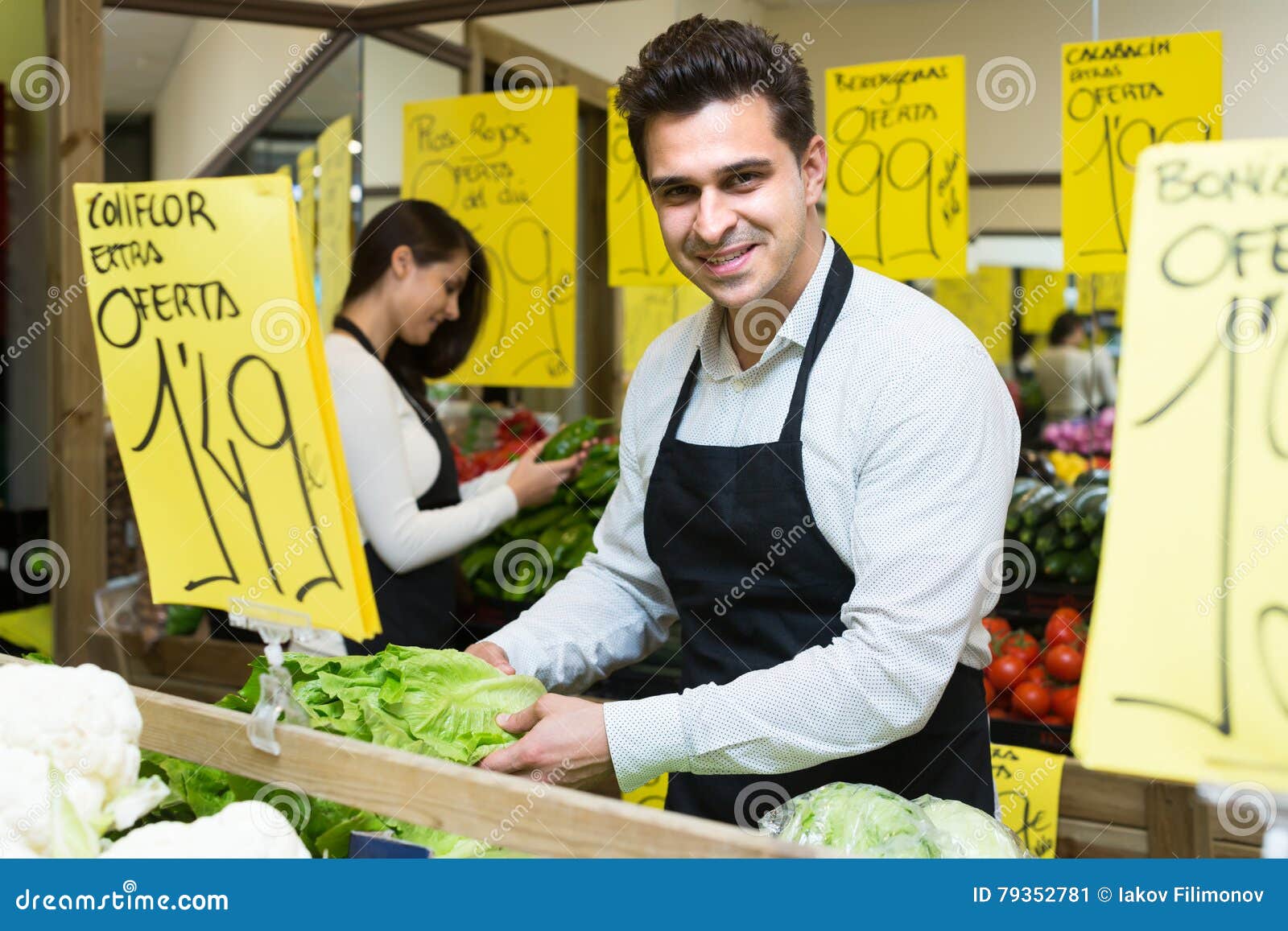 Seller with vegetables in market. Smiling seller holding lettuce in vegetables market, prices on Spanish