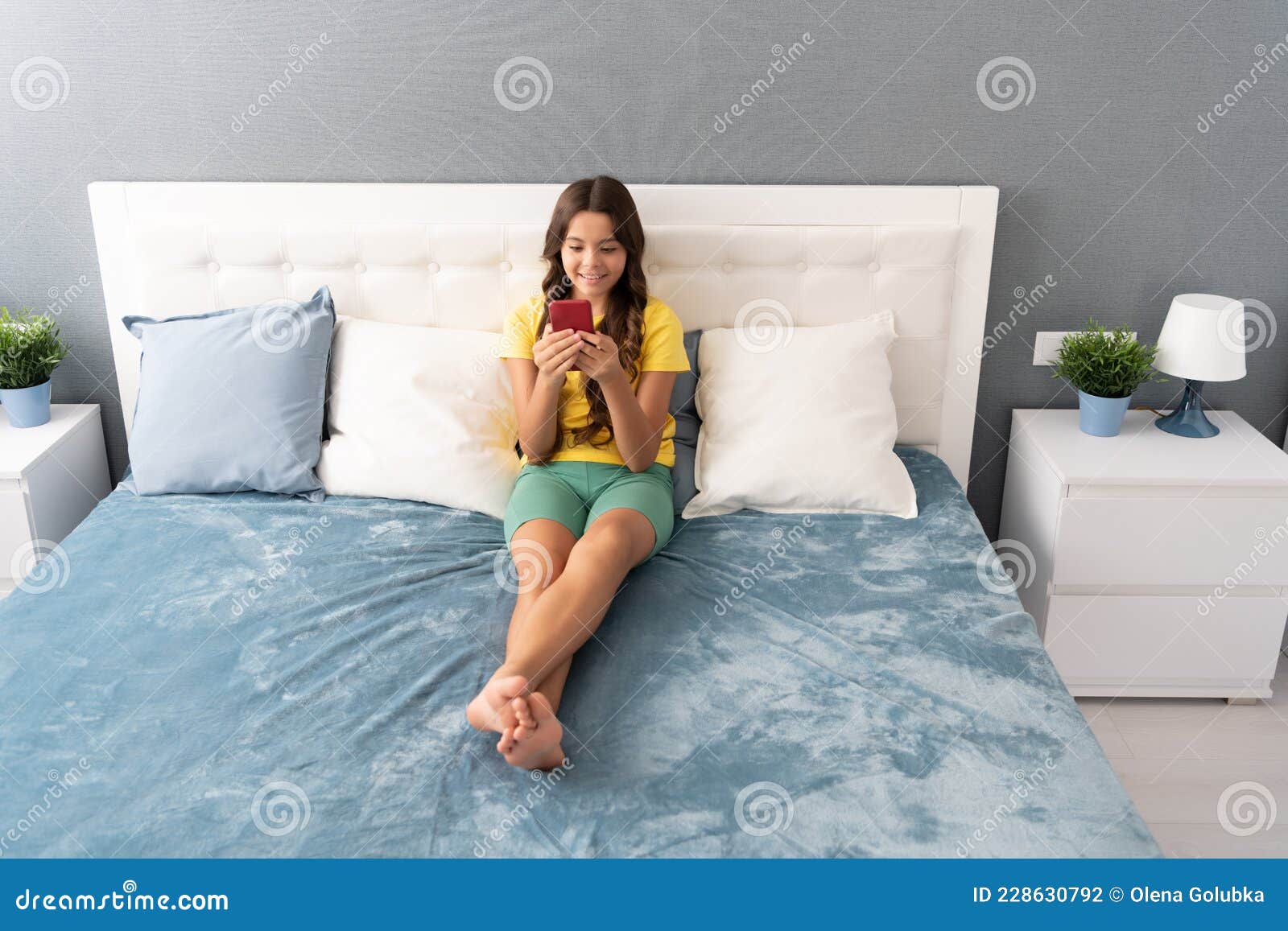 sending text message. child type sms sitting on bed. texting on mobile phone. sms