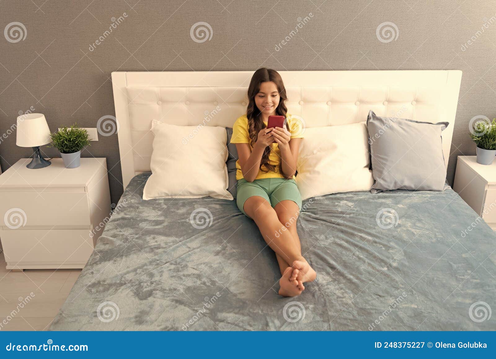 sending text message. child type sms sitting on bed. texting on mobile phone. sms
