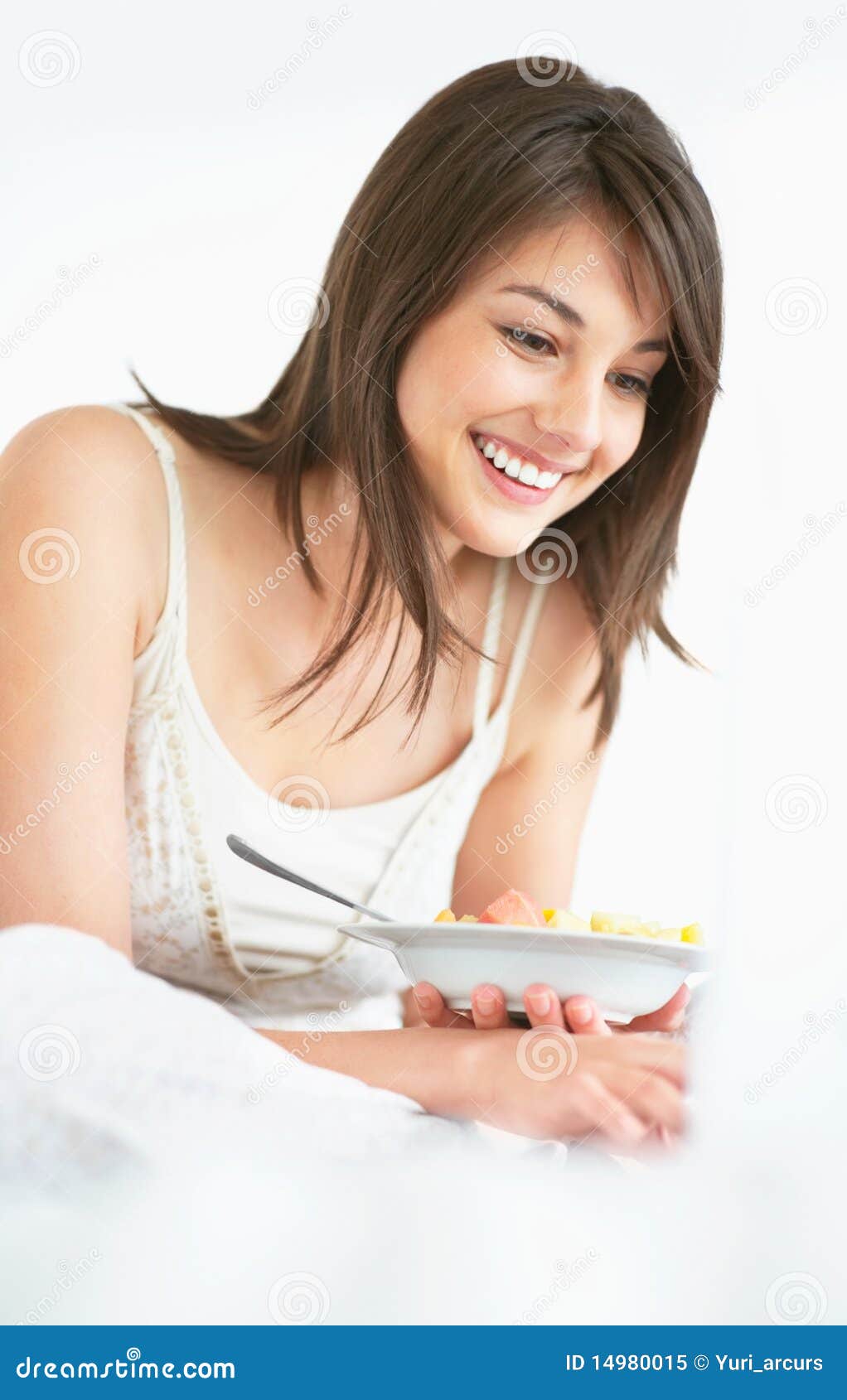 Senhora nova que usa um portátil e comendo a salada de fruta. Retrato de uma senhora nova feliz que usa um portátil e comendo a salada de fruta
