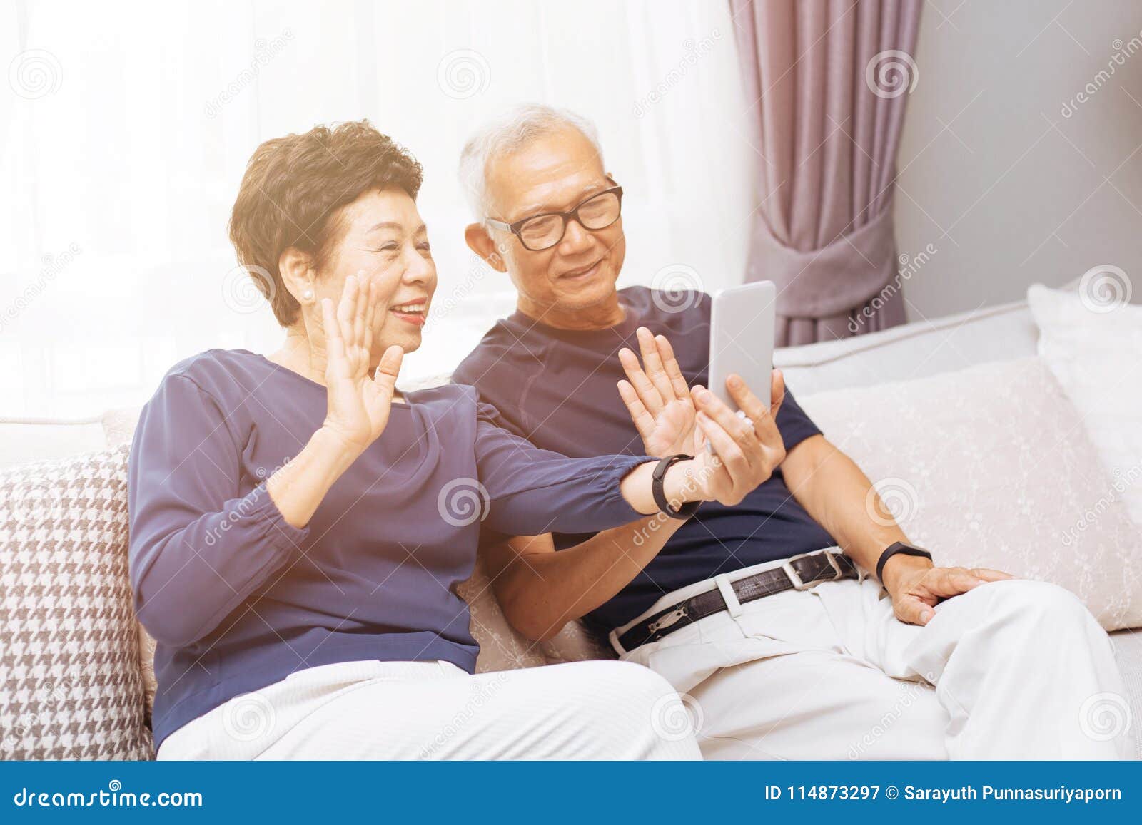 senior asian couple grand parents making a video call and waving at the caller.
