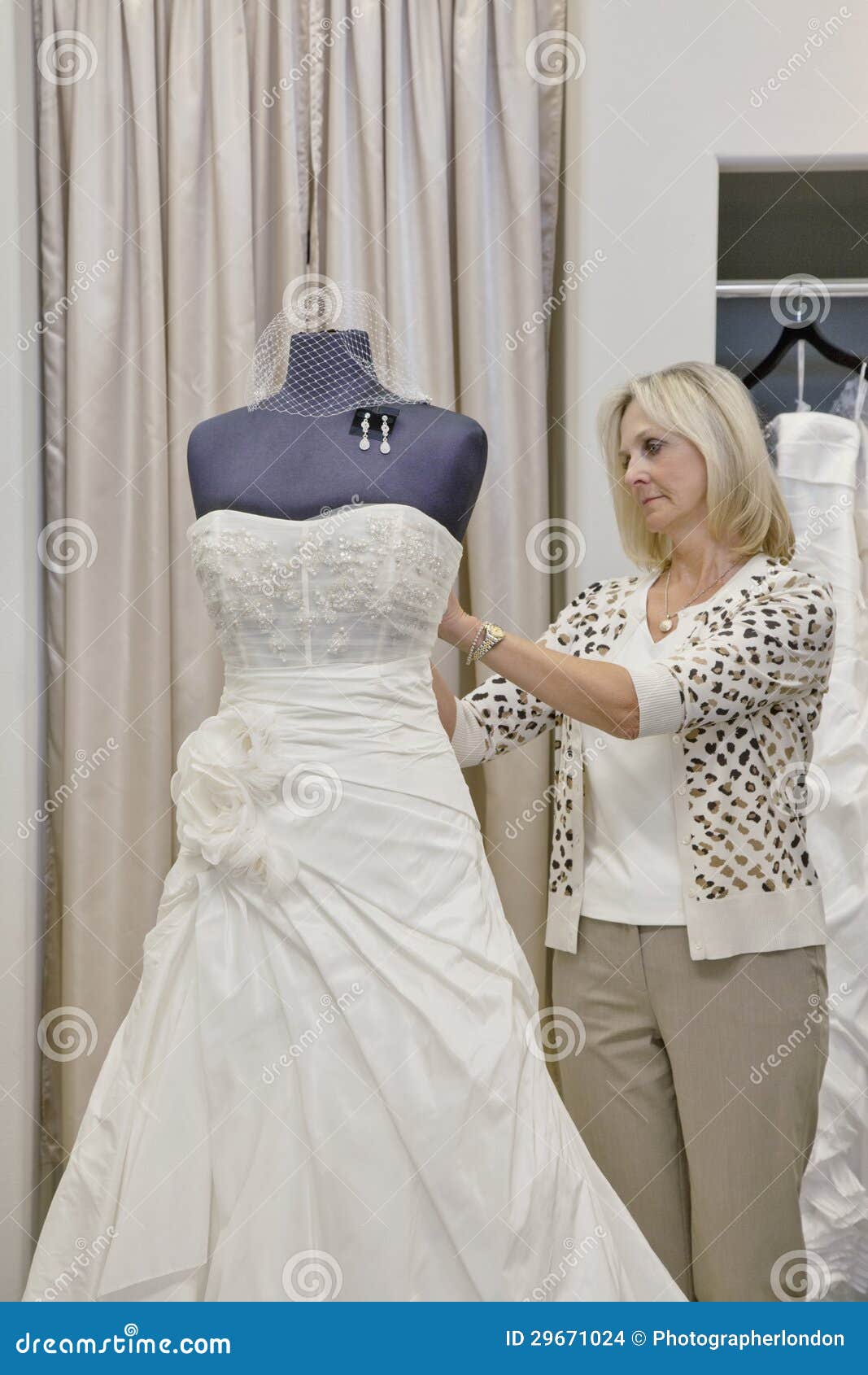 Senior Female Owner  Adjusting Wedding  Dress  On Mannequin 