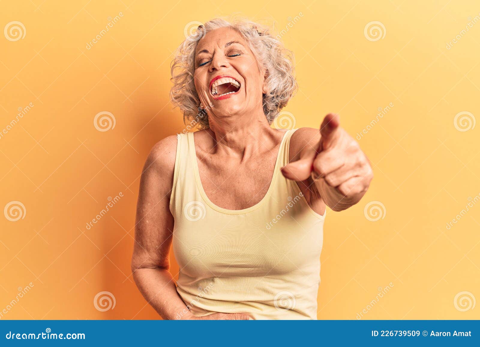 senior grey-haired woman wearing casual clothes laughing at you, pointing finger to the camera with hand over body, shame