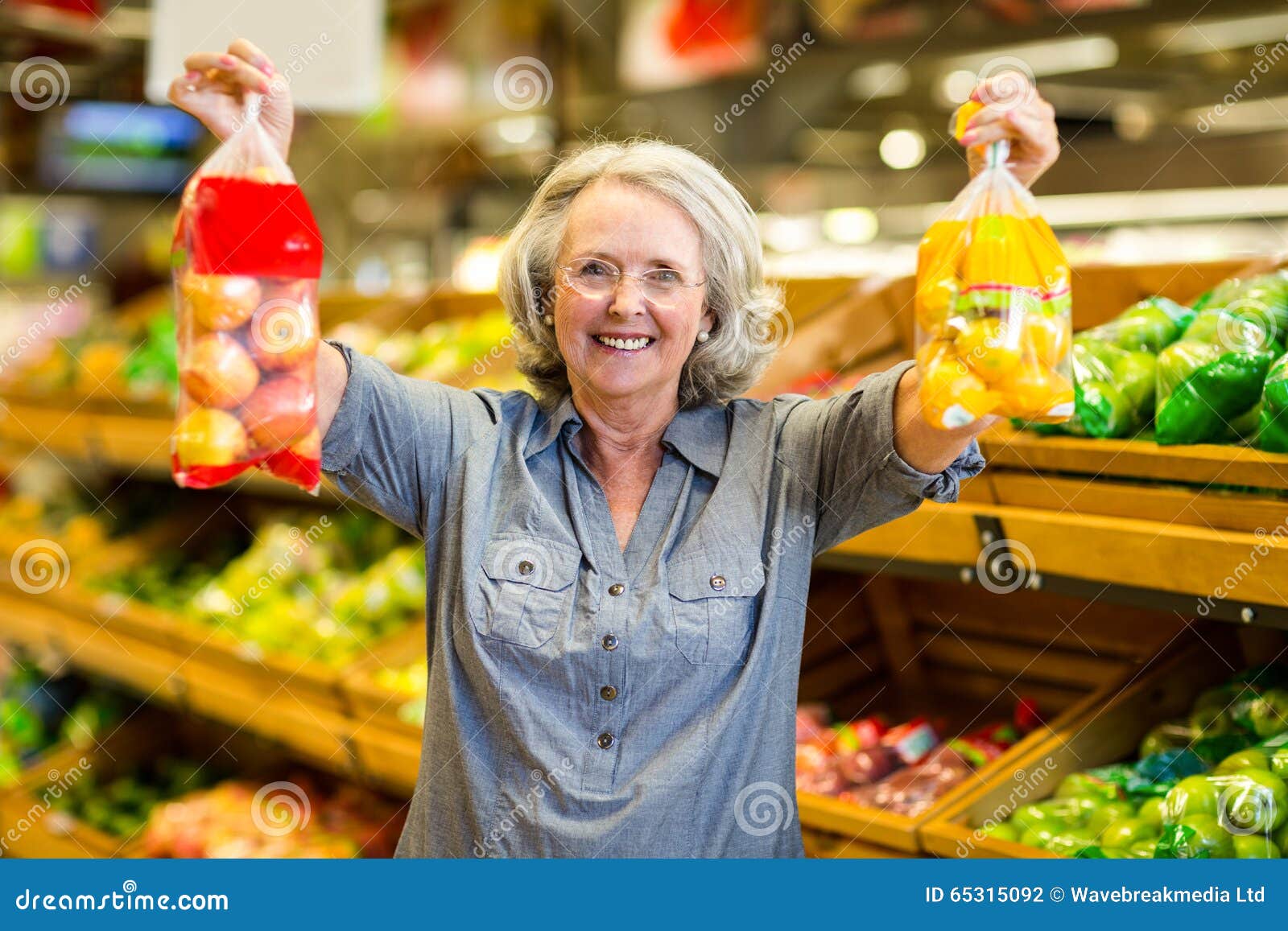 Senior happy woman holding bag of fruits in supermarket