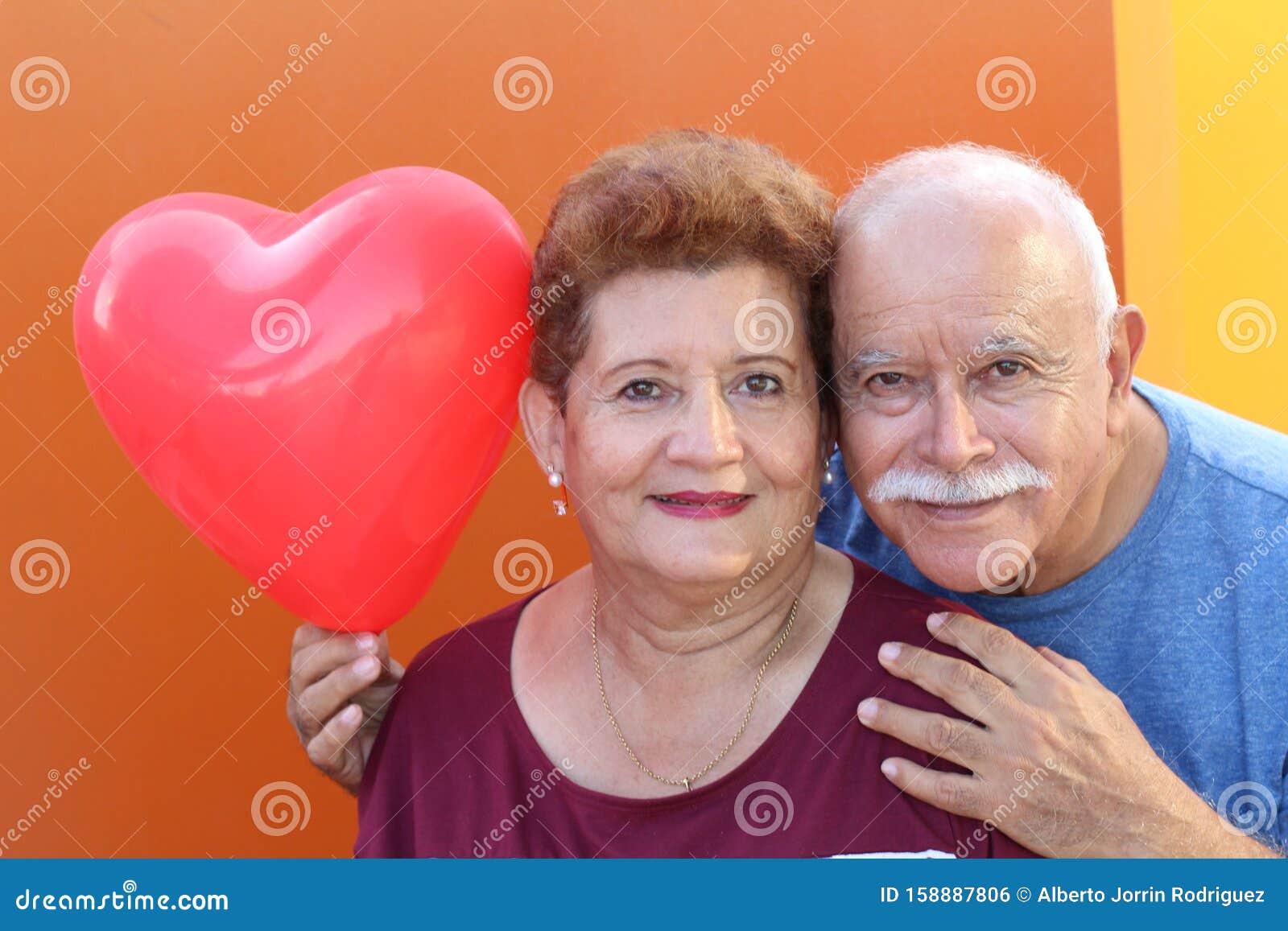 senior latino couple holding a heart balloon