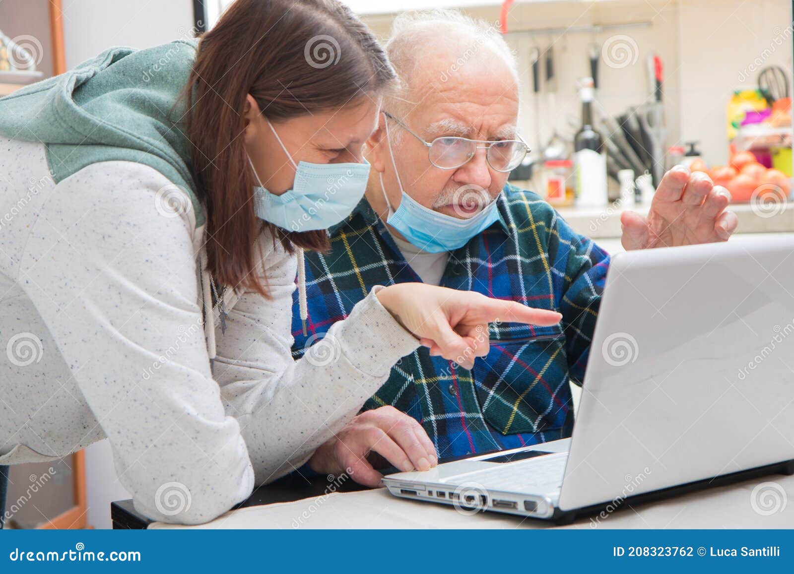 senior man is helped by his caregiver to using laptop at home during coronavirus pandemia