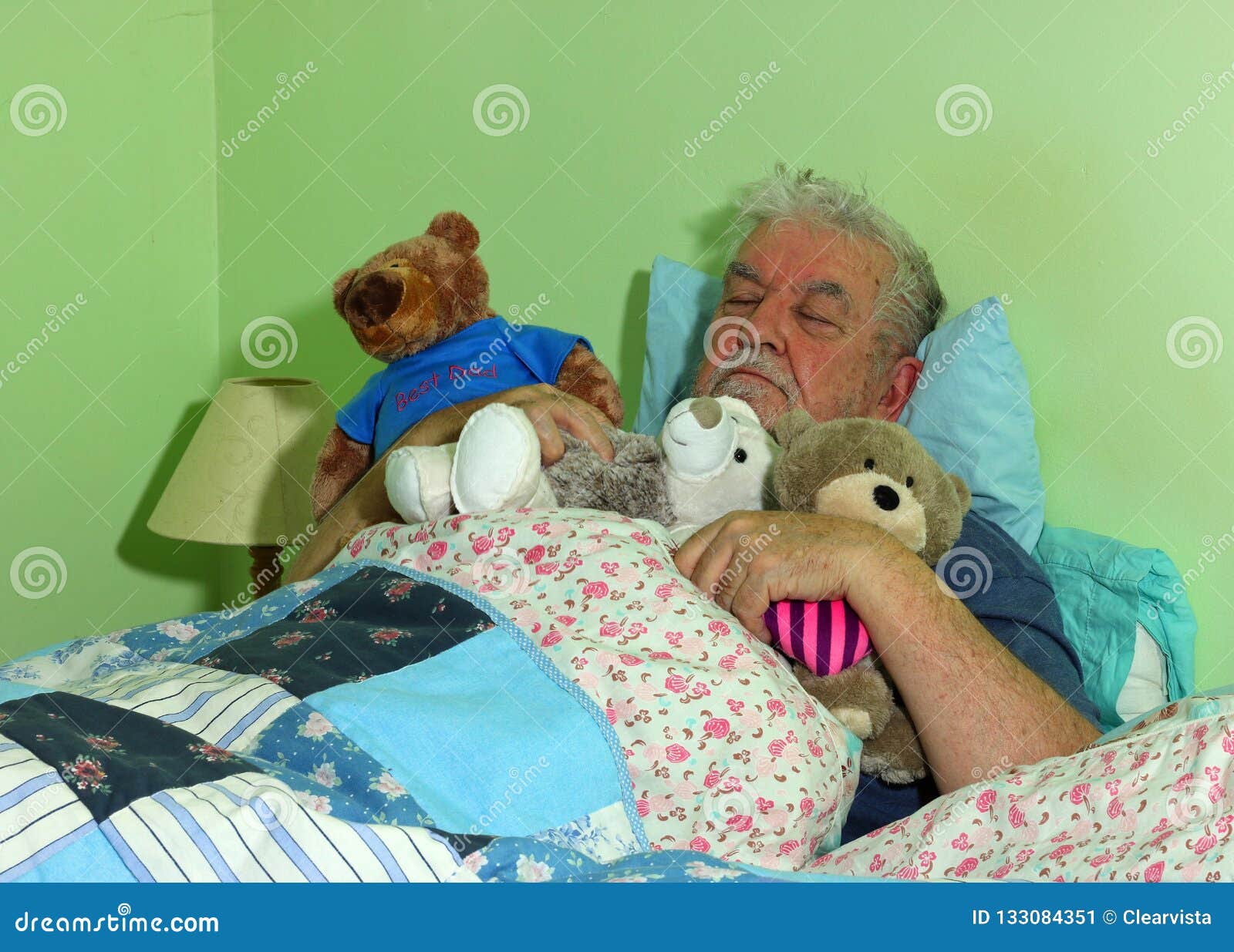 senior man asleep in bed with soft cuddly toys.