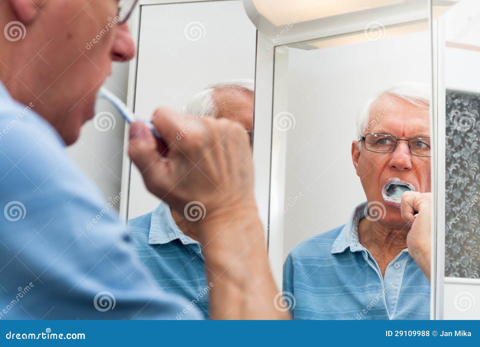 senior man in mirror brushing his teeth