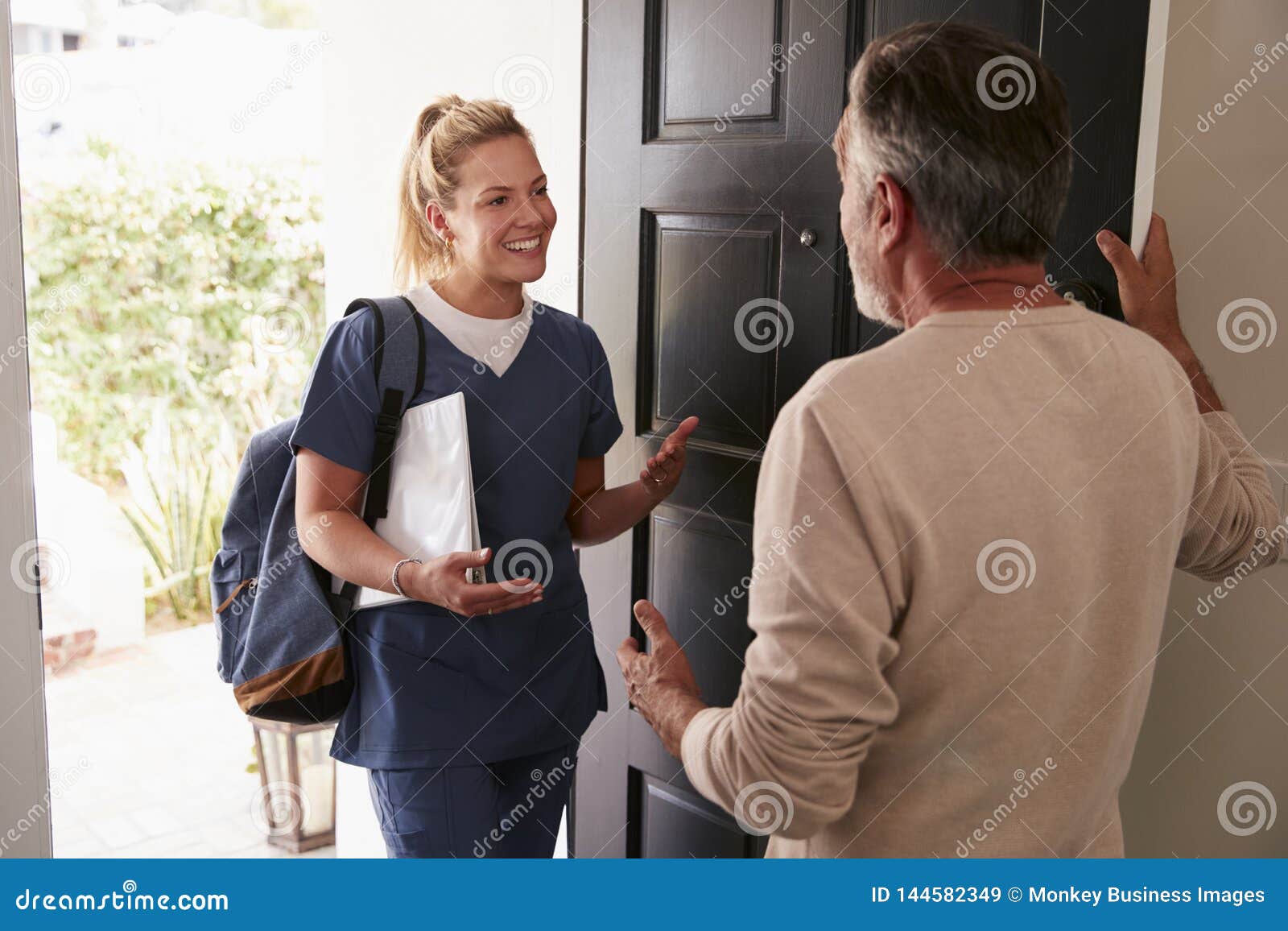 senior man opening his front door to a female healthcare worker making a home health visit