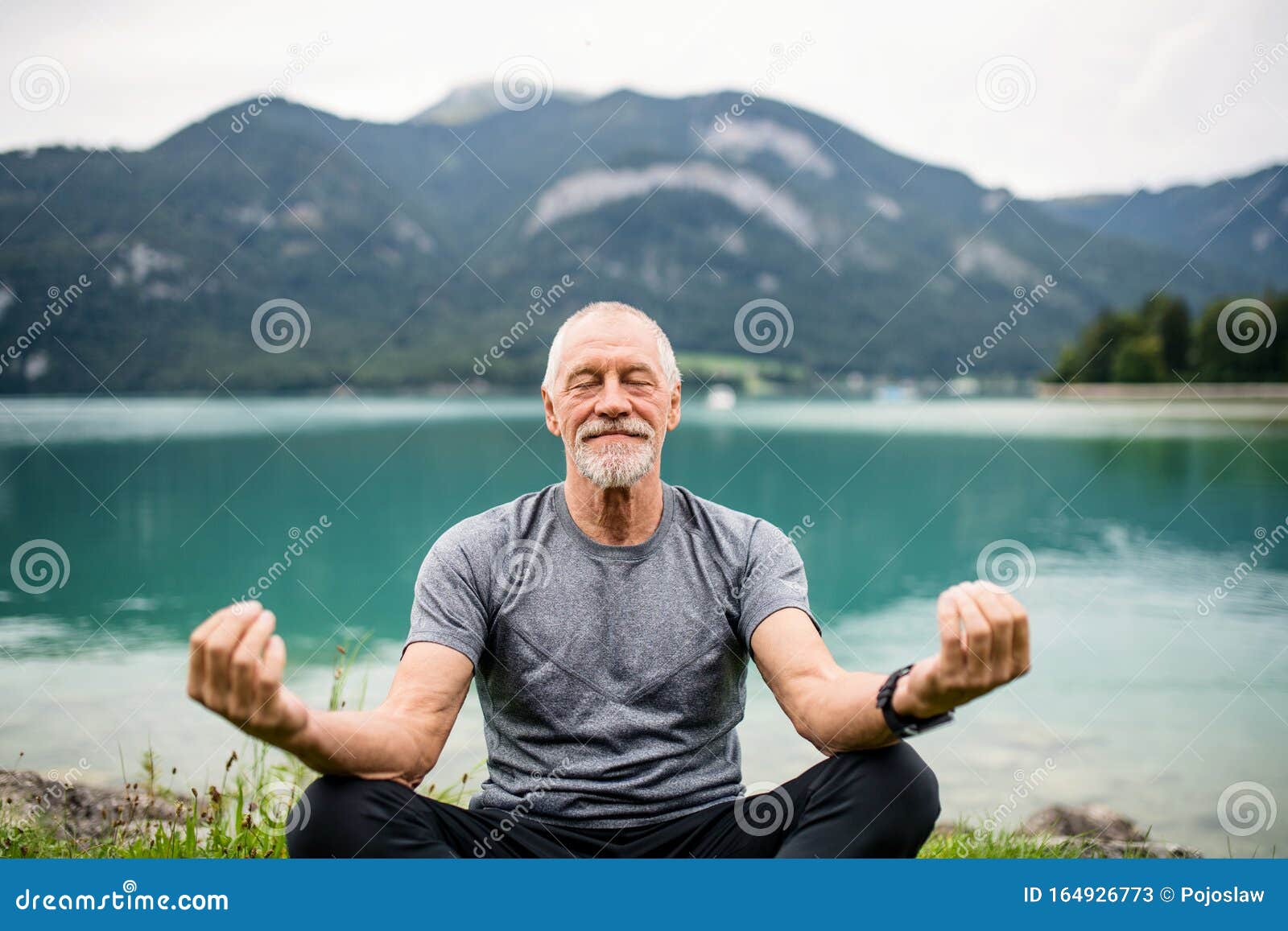 a senior man pensioner sitting by lake in nature, doing yoga exercise.