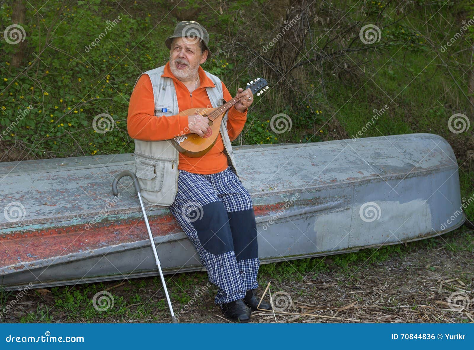 senior man sitting on an old reversed boat and singing
