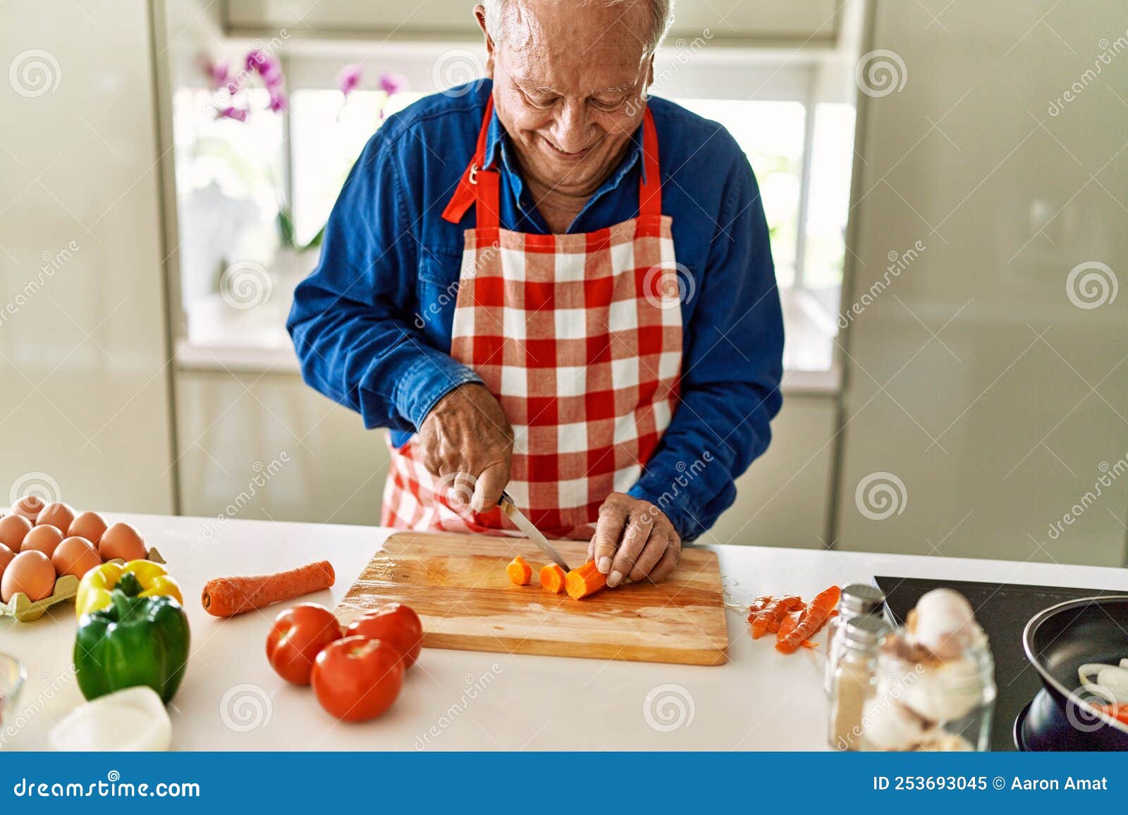 senior man smiling confident cutting carrot at kitchen