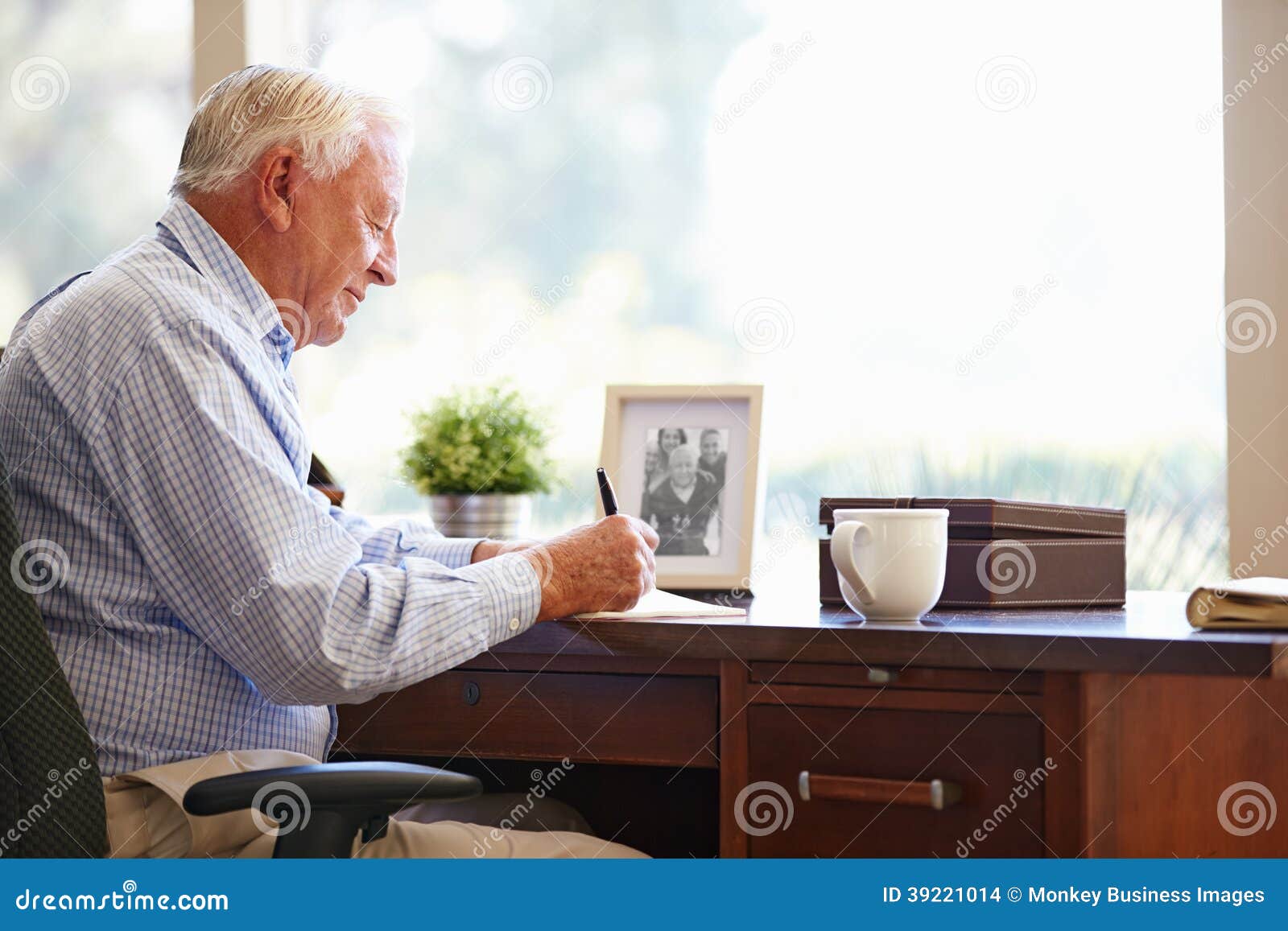 senior man writing memoirs in book sitting at desk