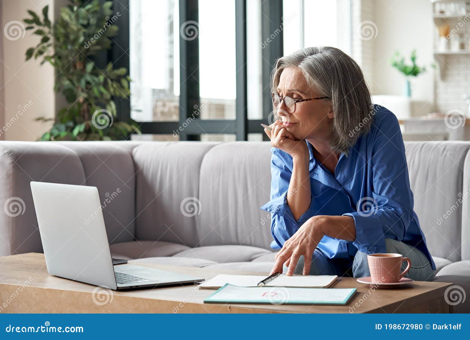 senior older woman watching webinar on laptop working from home.