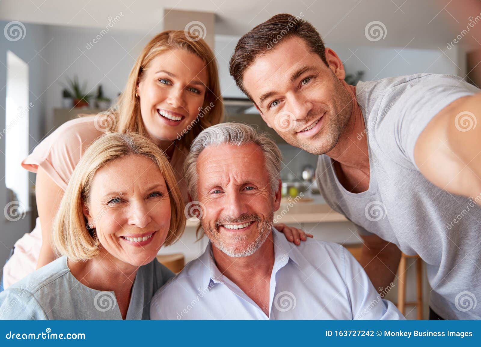 senior parents with adult offspring posing for selfie at home