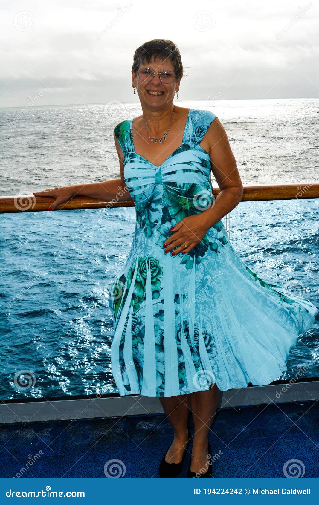 Mature Woman Stands on Deck of Cruise Ship As it Heads Out To Sea Stock