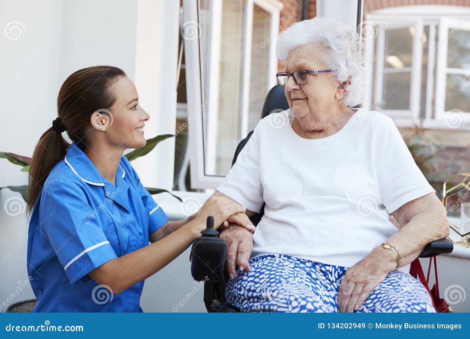 senior woman sitting in motorized wheelchair talking with nurse in retirement home