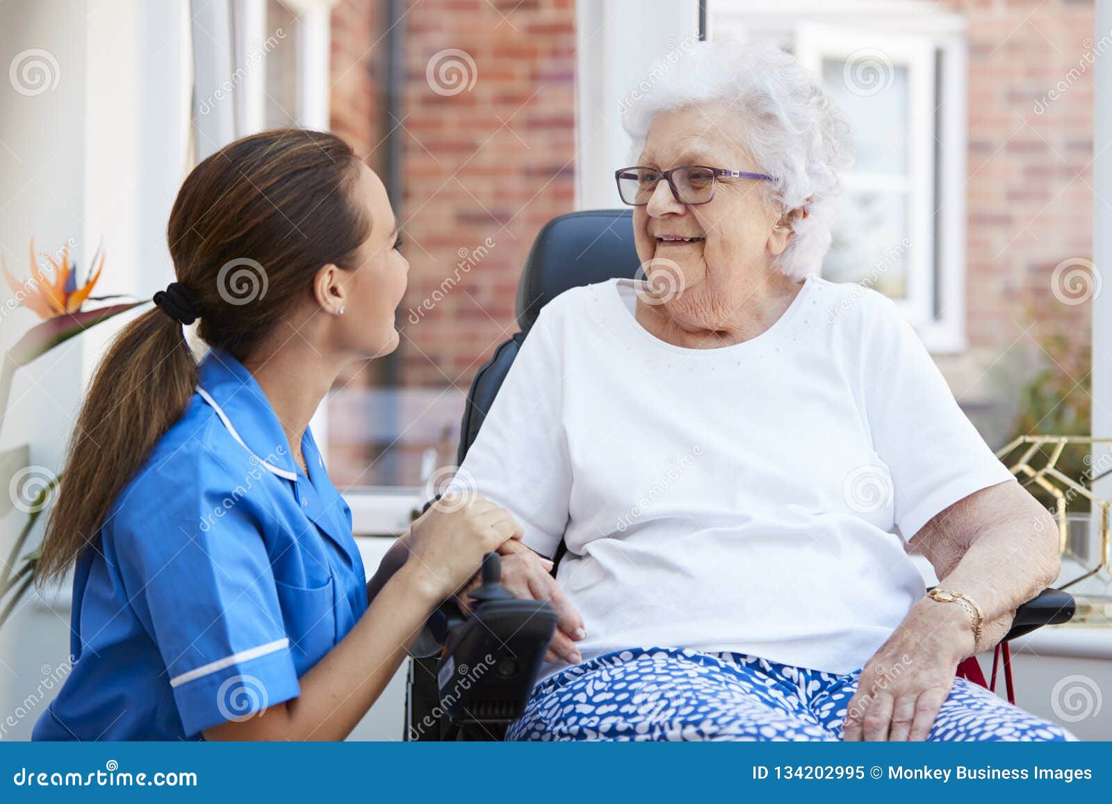 senior woman sitting in motorized wheelchair talking with nurse in retirement home