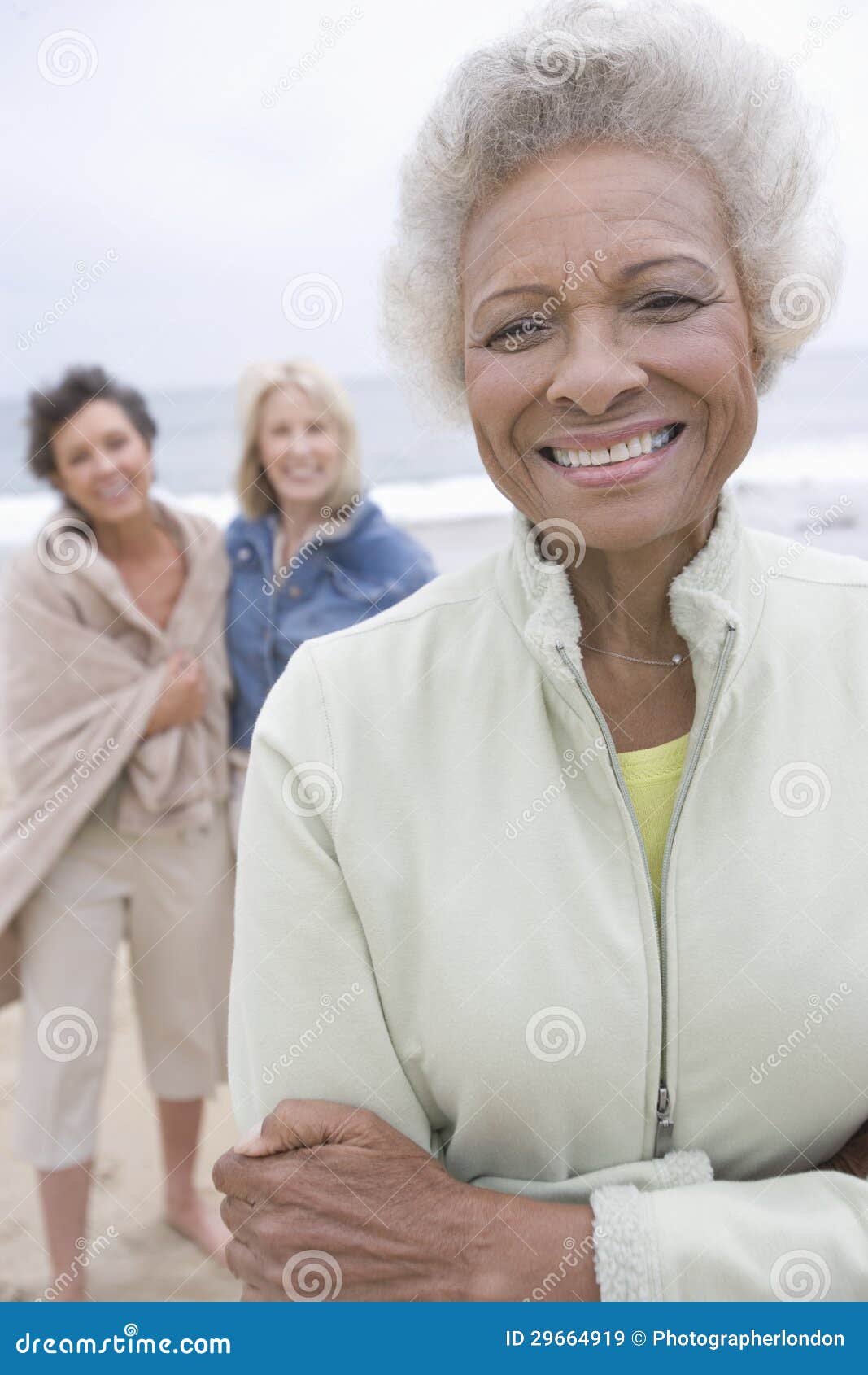 senior woman stands in fleece jacket with friends on beach