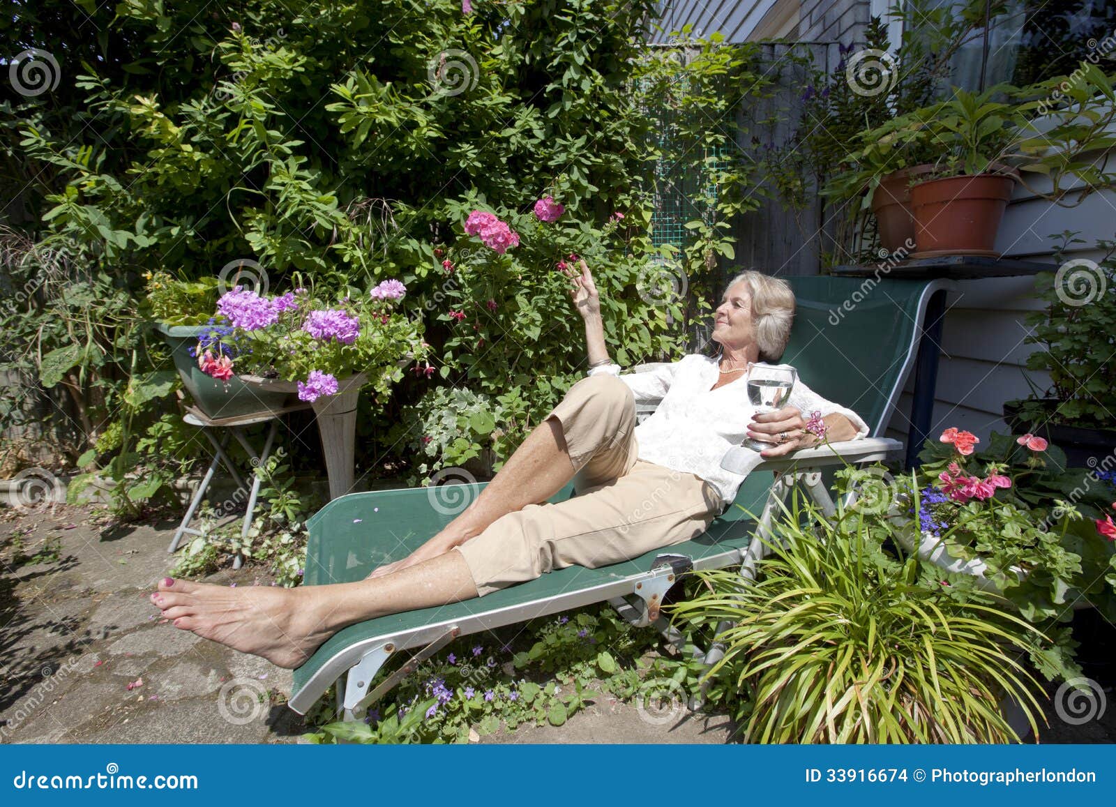 Senior Woman With Wineglass Relaxing On Lounge Chair In Garden Stock