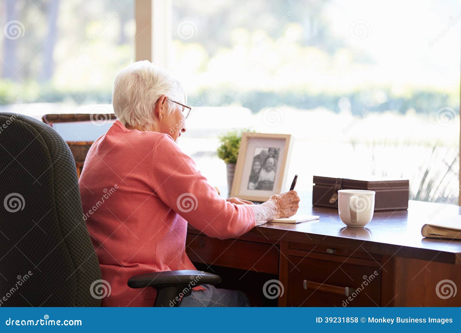 senior woman writing memoirs in book at desk