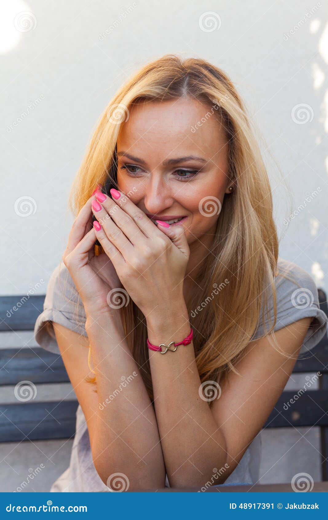 sensual blonde woman sitting on wooden bench. she is using mobile phone