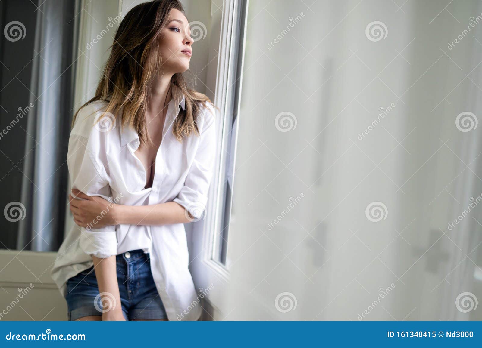 Sensual Brunette Woman Standing Near The Window In White Shirt Stock