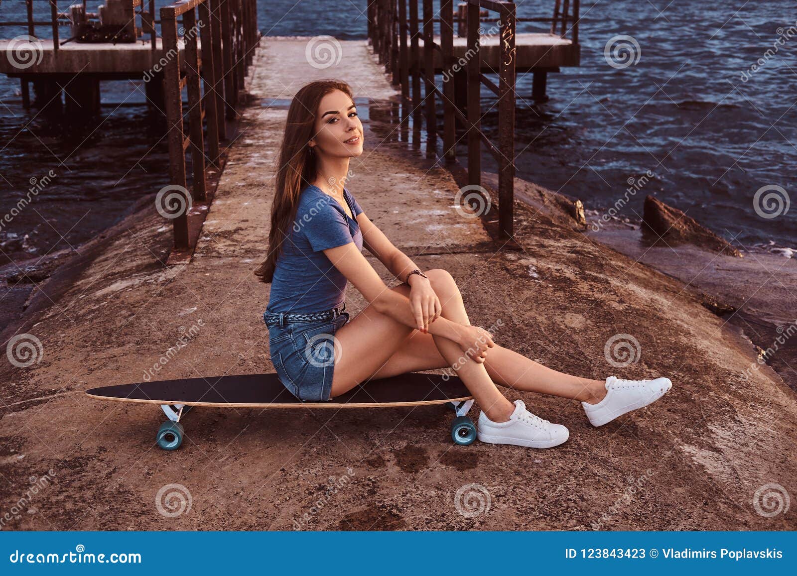 Portrait Of A Girl Sitting On A Skateboard On The Old Pier Is Enjoying Amazing Dark Cloudy 