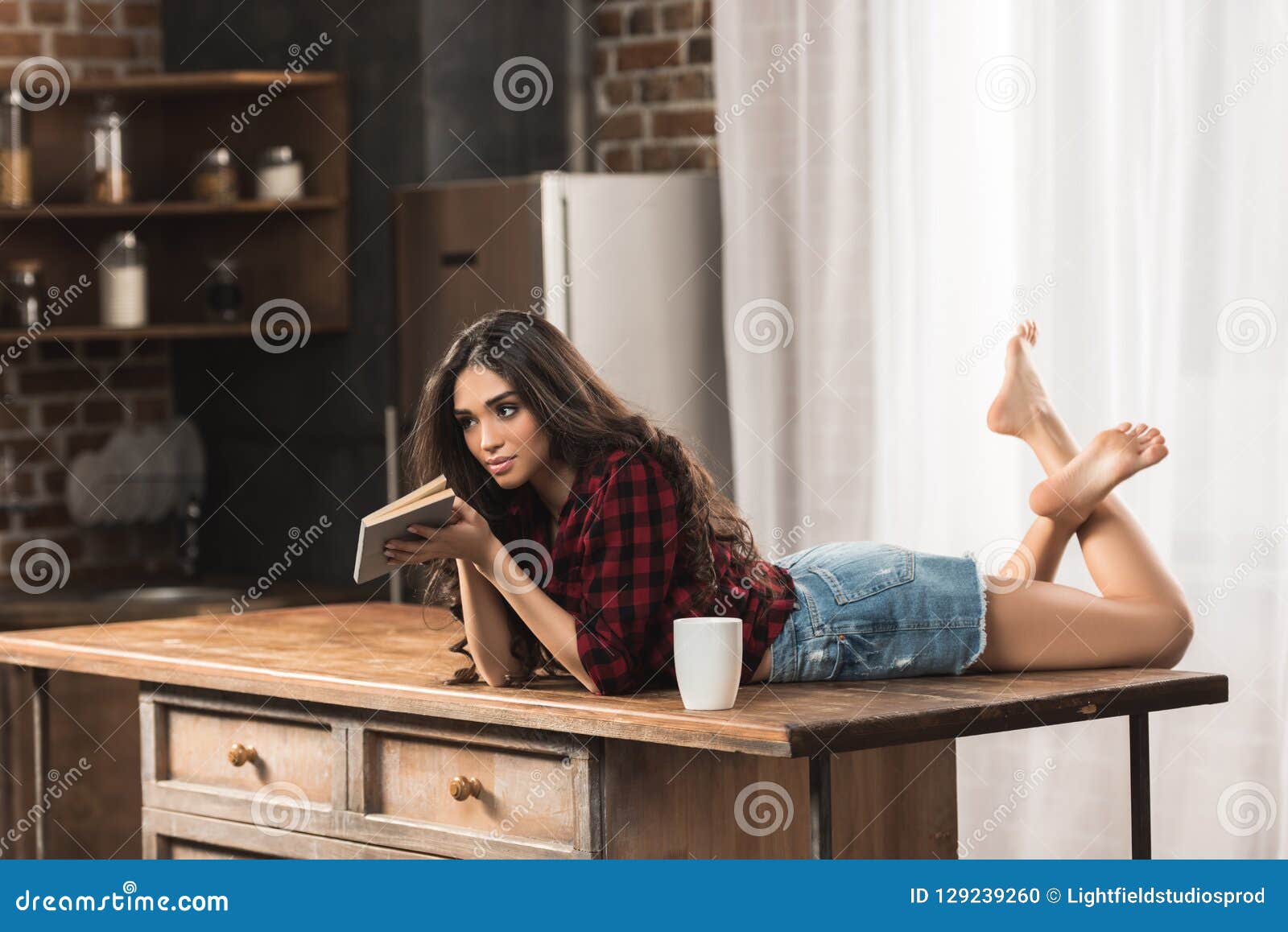 sensual young woman with book lying on table with cup