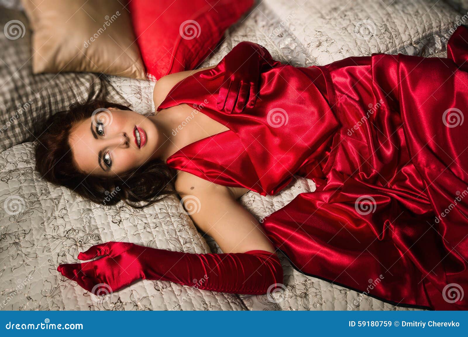Sensueel Brunette In Een Rode Kleding Die Op Het Bed Liggen Stock